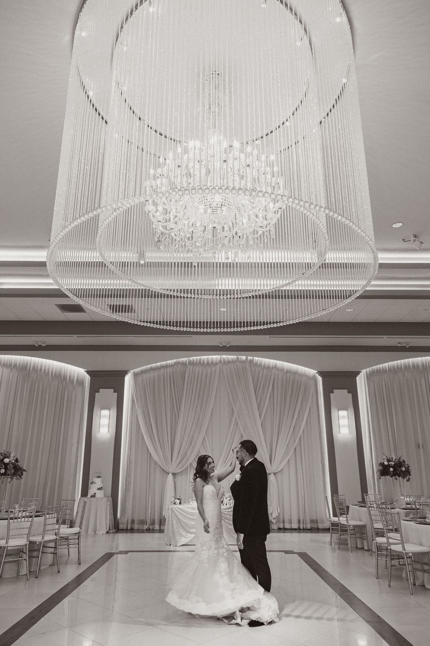 Monochrome wedding scene featuring crystal chandelier and elegant draped ballroom decor.
