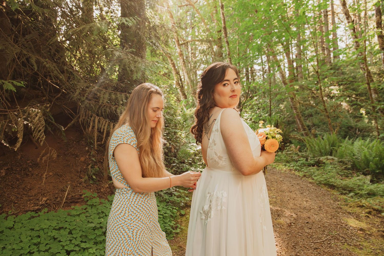Two people share joyful laughter while walking along a sunlit forest trail.