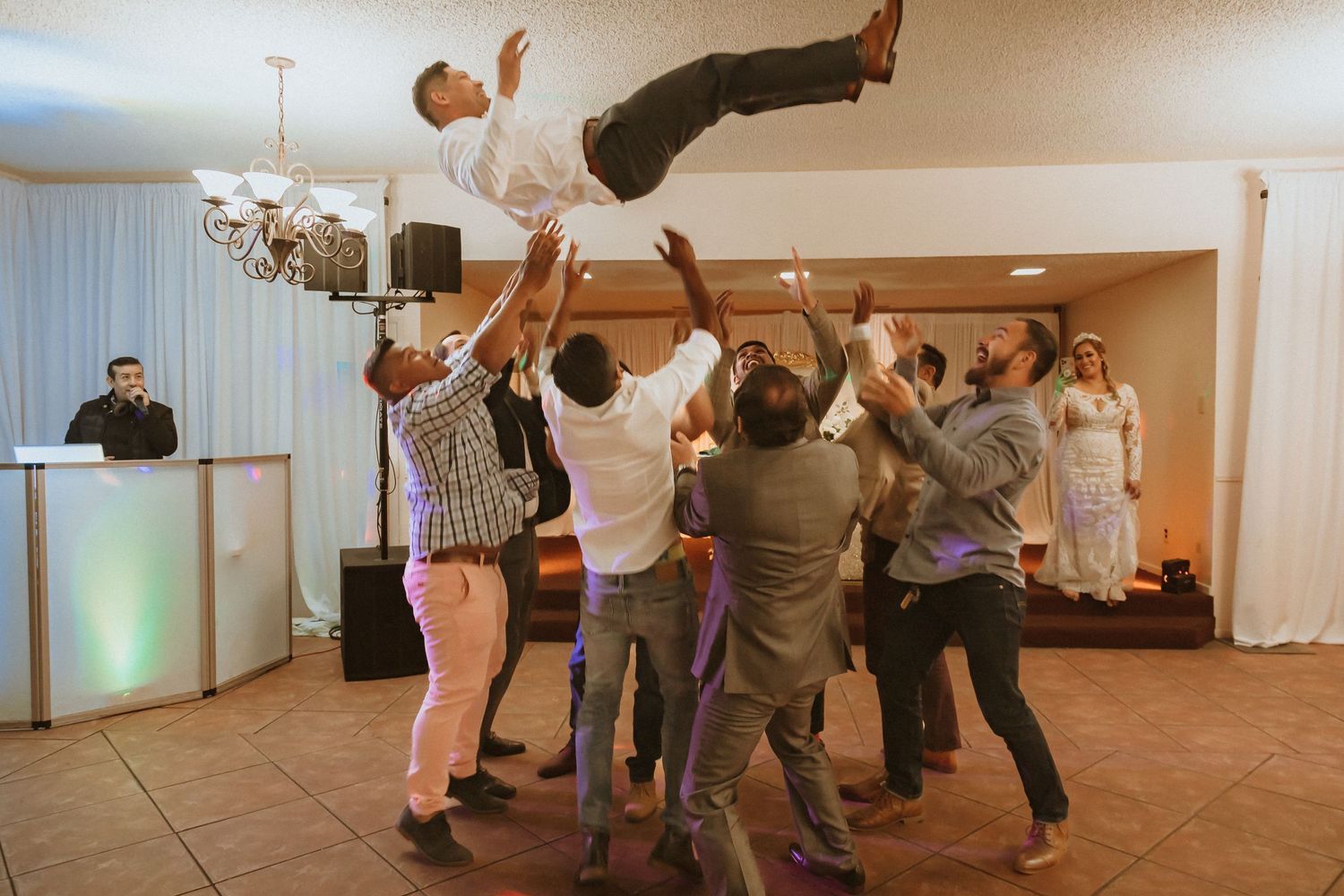 Wedding guests coordinate to lift and toss someone during a reception celebration.
