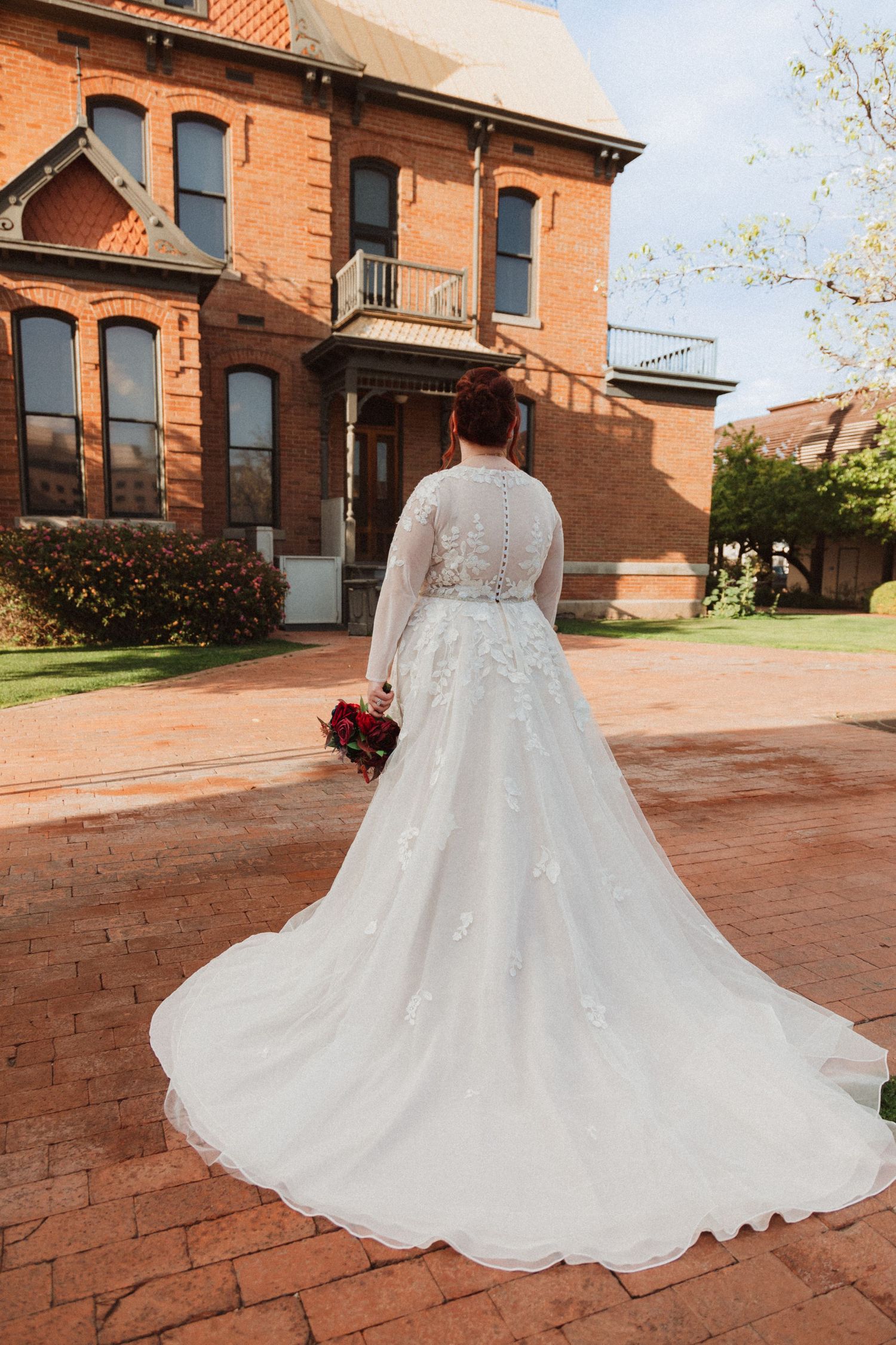 Back view of bride in lace wedding gown with long train in front of historic brick mansion.