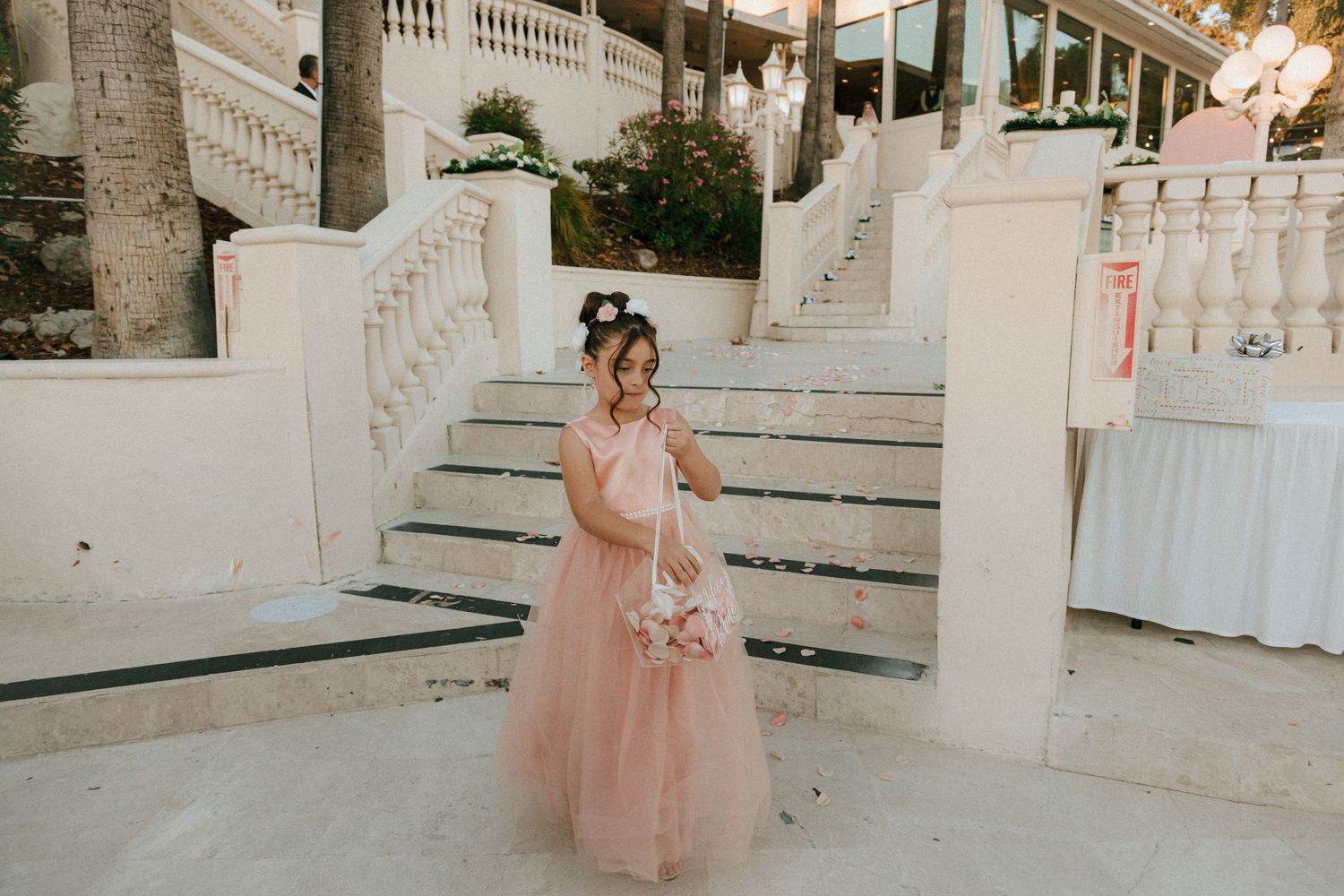 Person in pink tulle dress twirls on grand white staircase with palm trees.