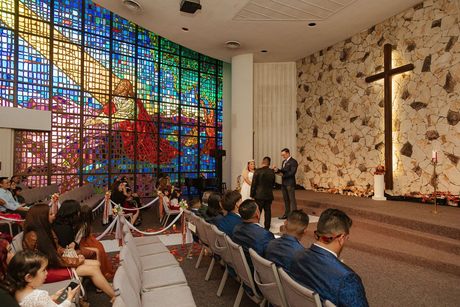 Church interior with colorful stained glass windows and stone walls during a wedding ceremony.