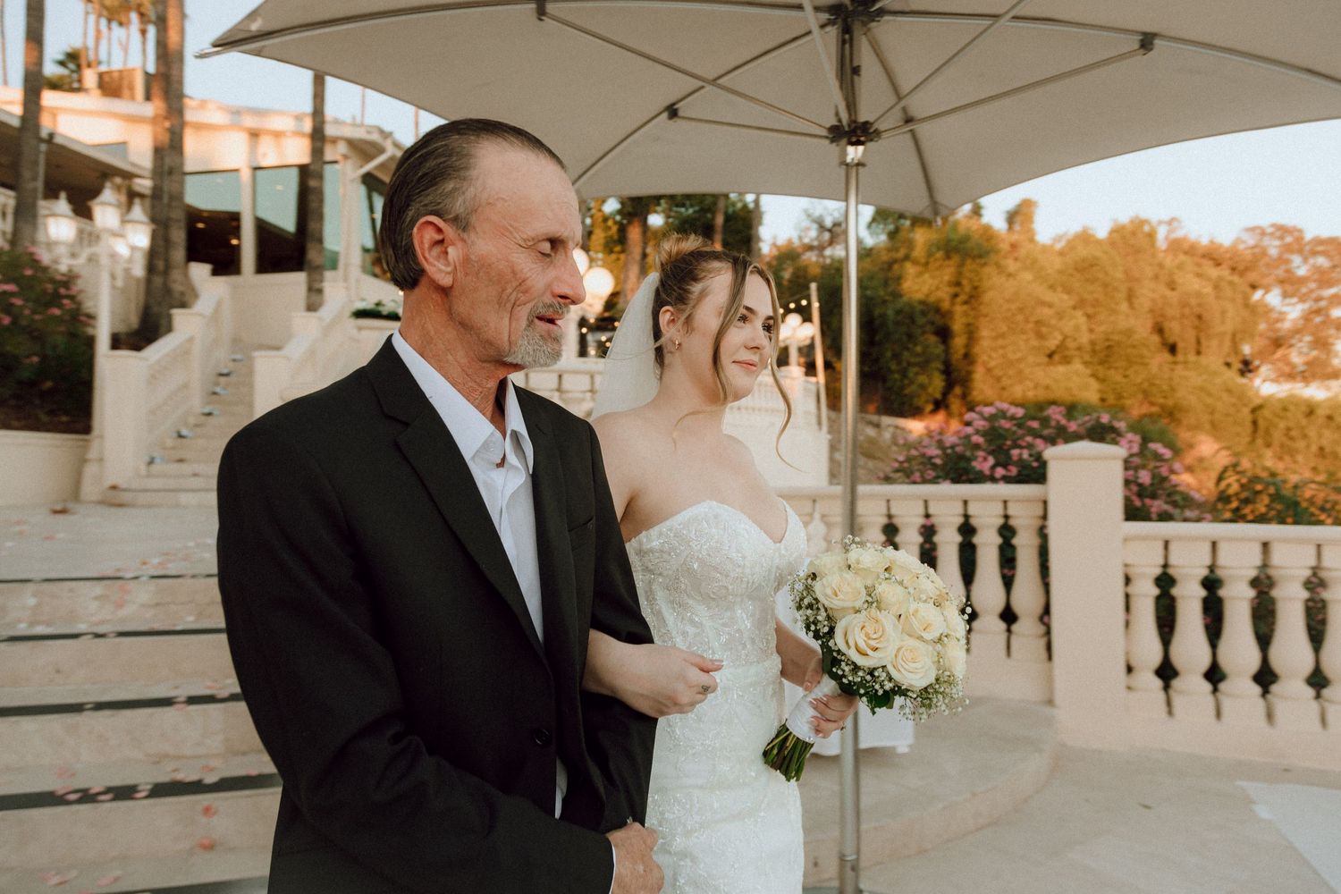 A couple shares a tender moment under an umbrella on an elegant terrace during golden hour.