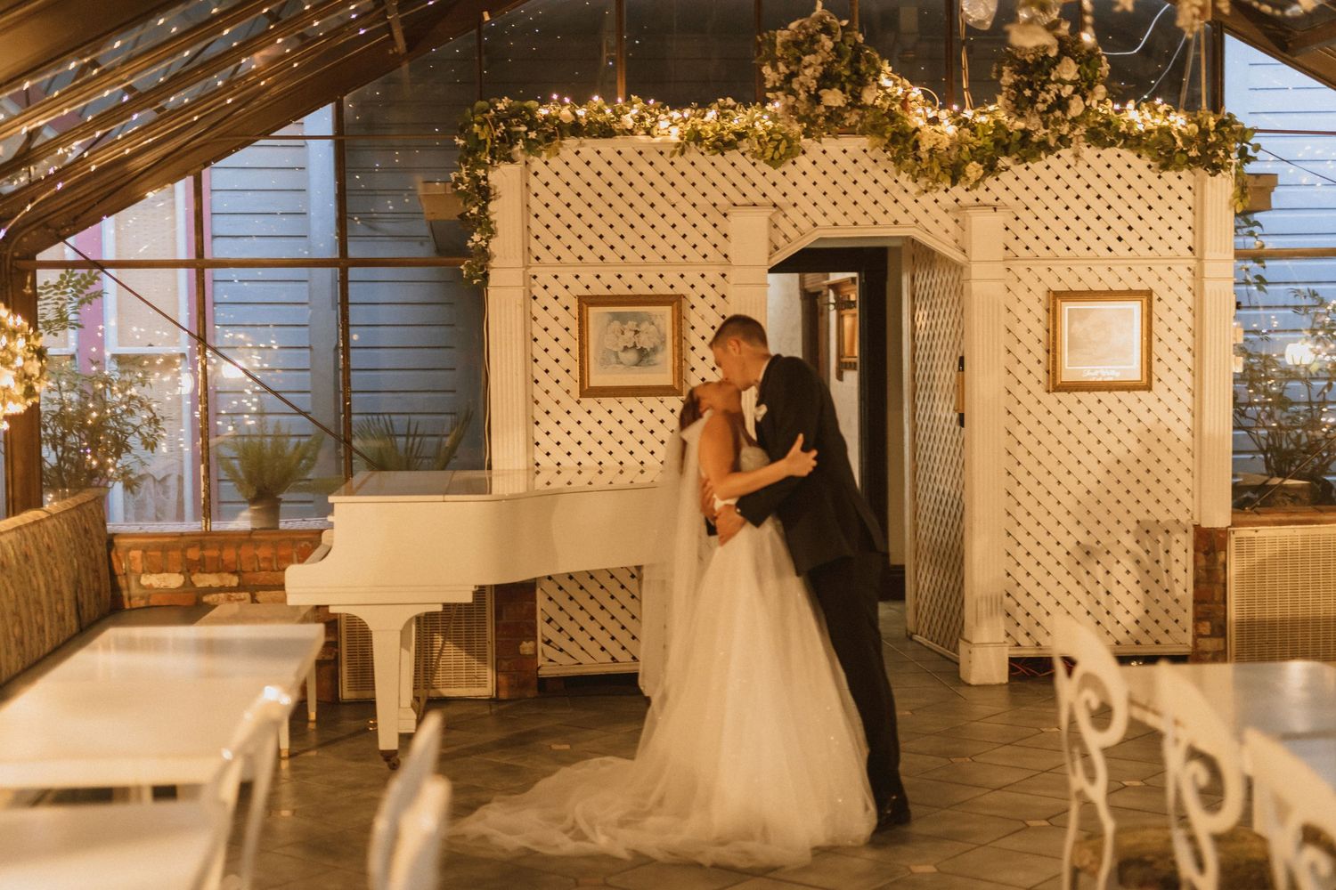Warm-toned wedding photo capturing romantic moment under lattice arch decorated with fairy lights.