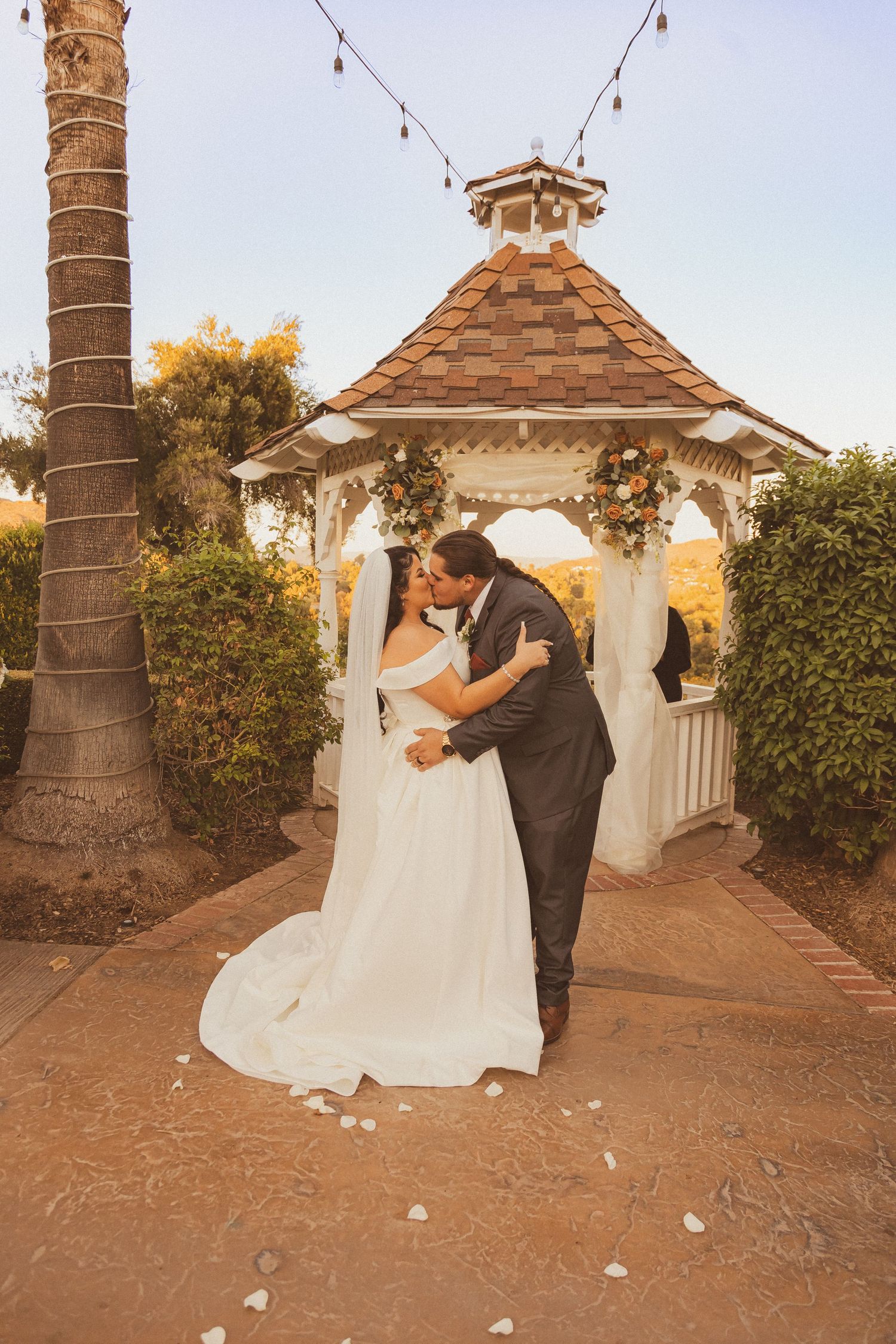 A romantic moment captured under a wooden gazebo with string lights overhead.