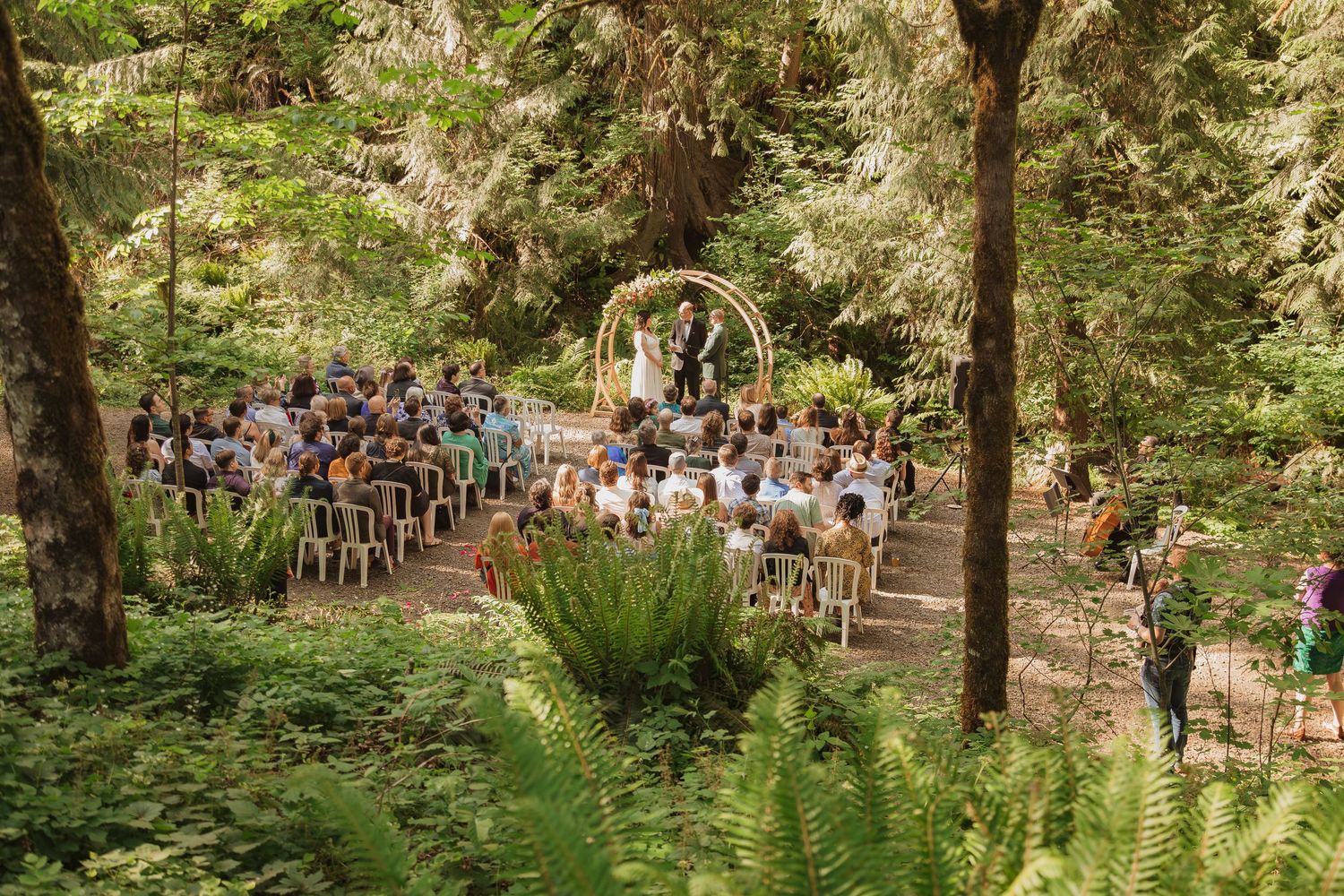 Aerial view of woodland wedding ceremony with guests seated before a round floral arch.