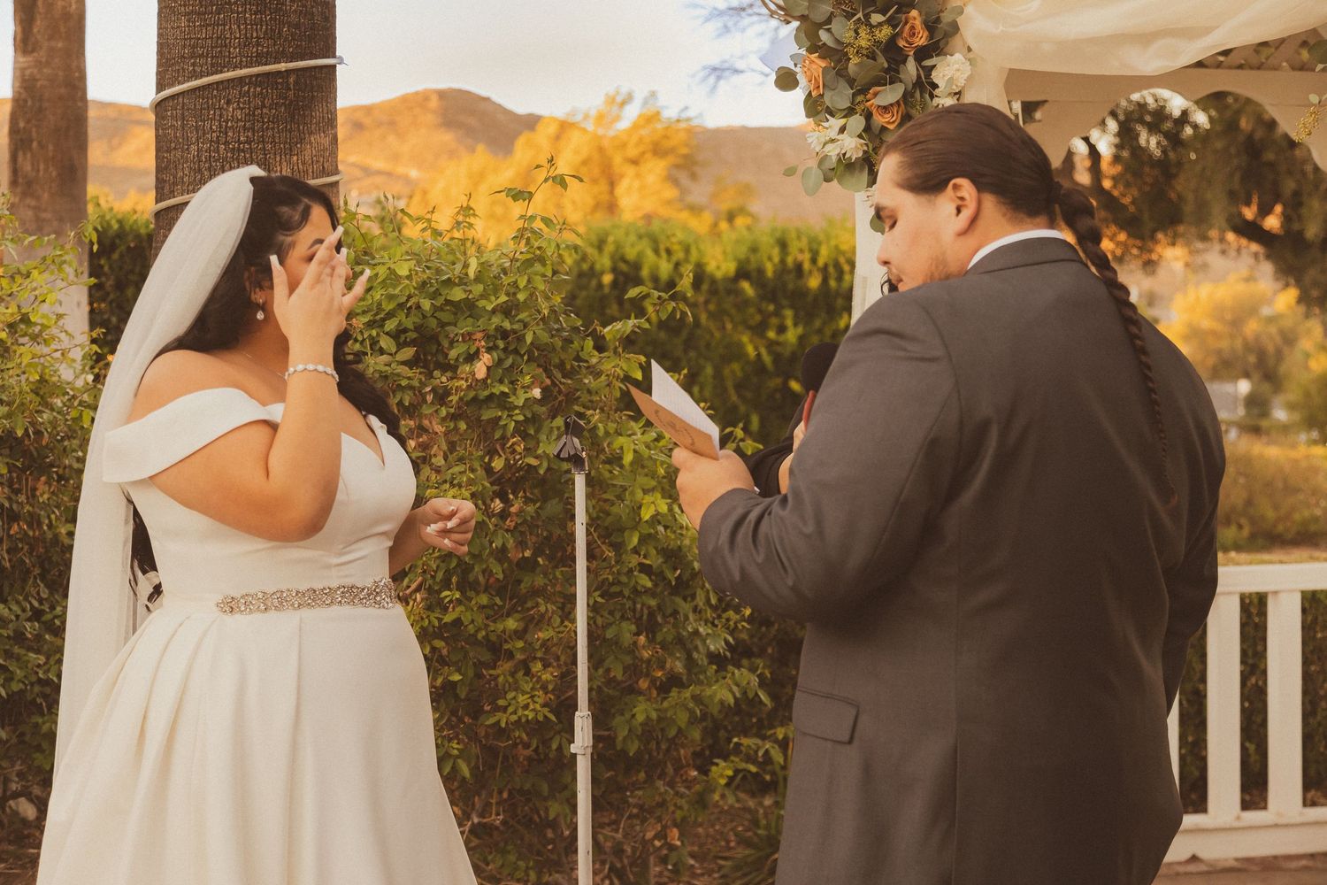 Emotional moment during wedding vow exchange at sunset outdoor ceremony.
