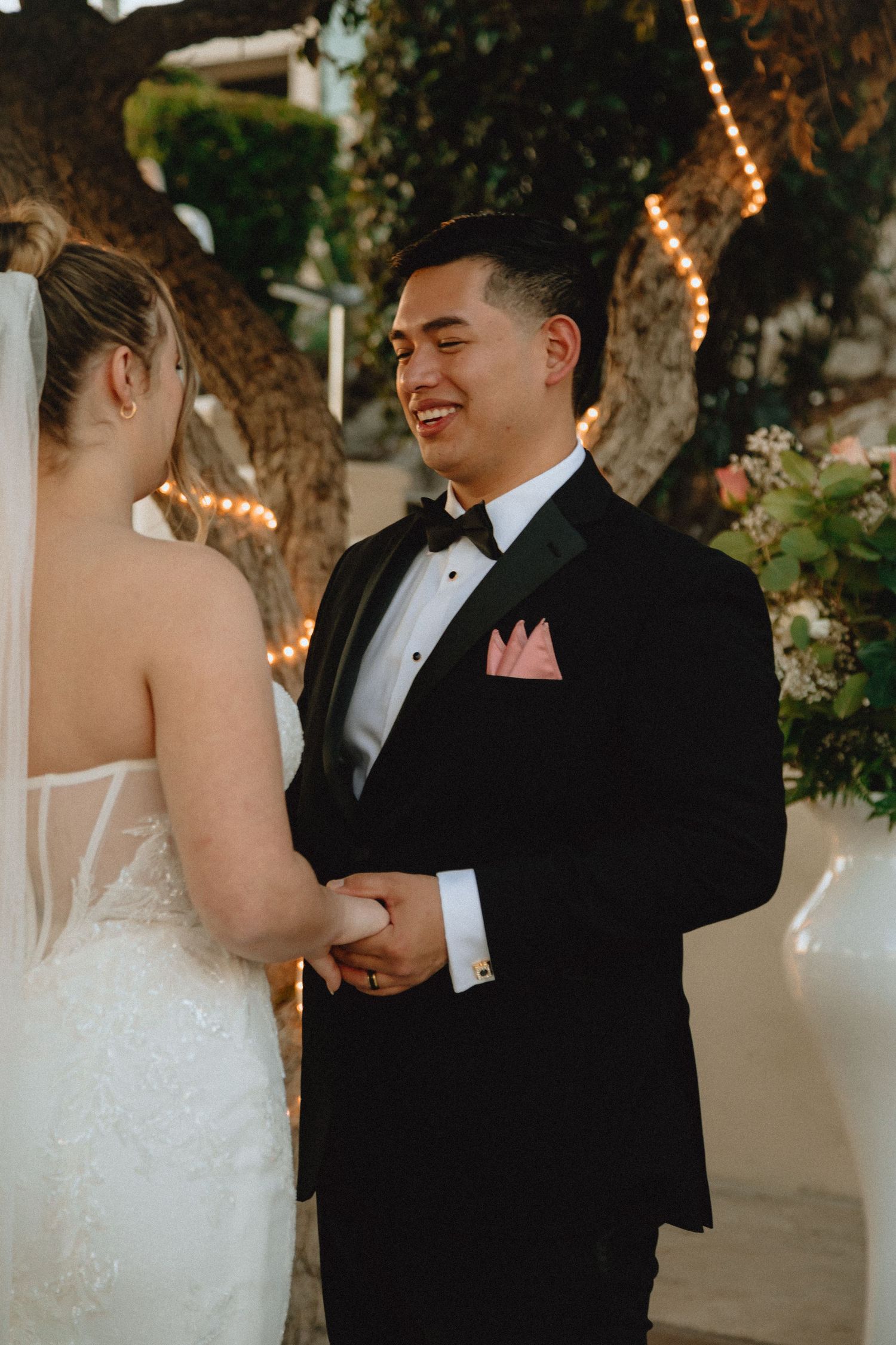 Joyful moment shared during outdoor wedding ceremony under string-lit trees.