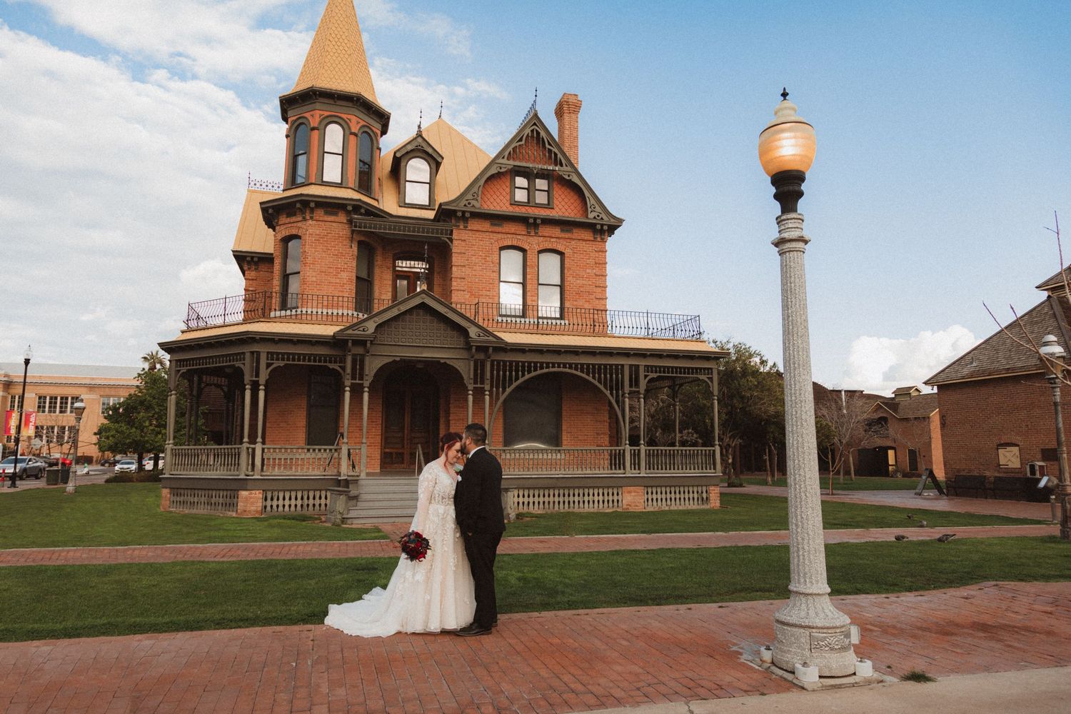 Wedding portrait in front of a historic Victorian mansion with decorative turret and lamp post.