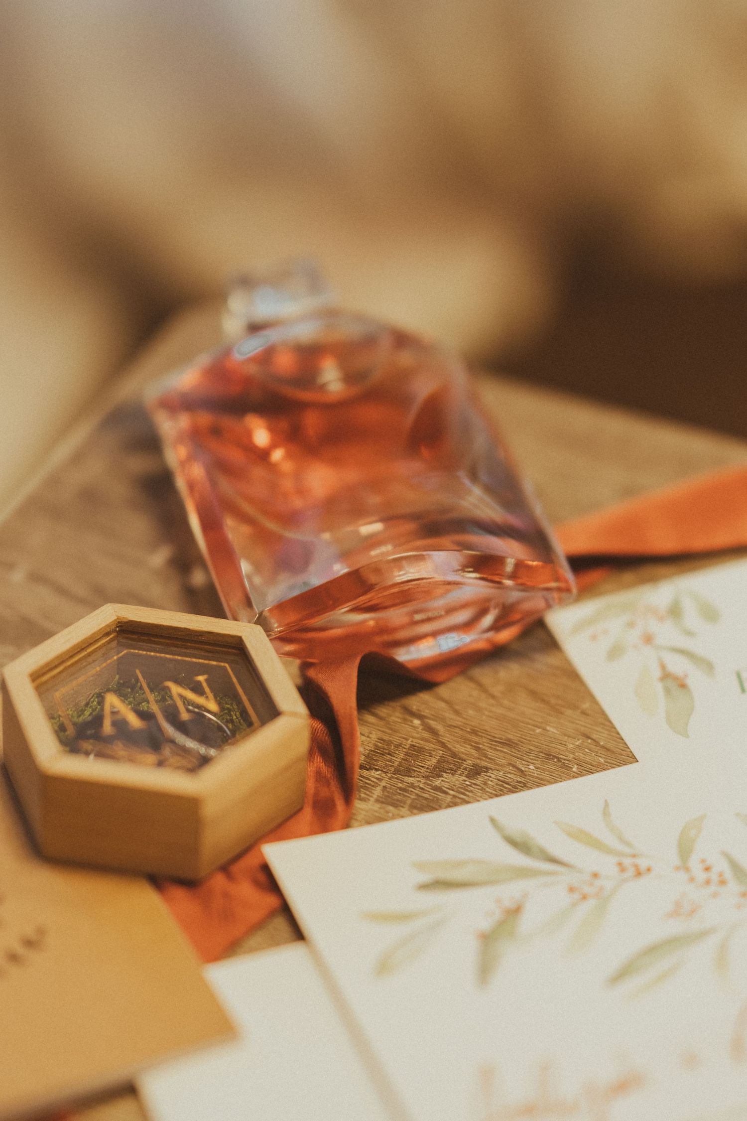 Close-up of perfume bottle, hexagonal box and wedding invitation with botanical details.