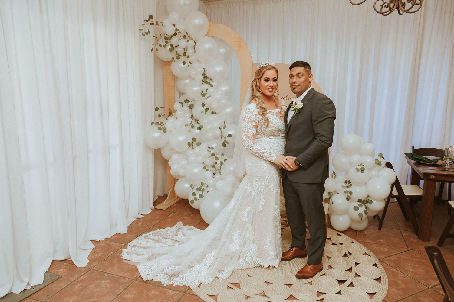 Wedding portrait in front of white balloon arch and floral decorations.