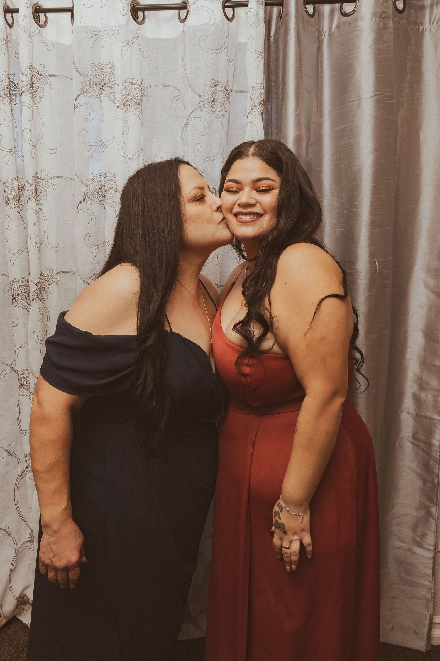 Two friends sharing a joyful moment against a curtained backdrop.