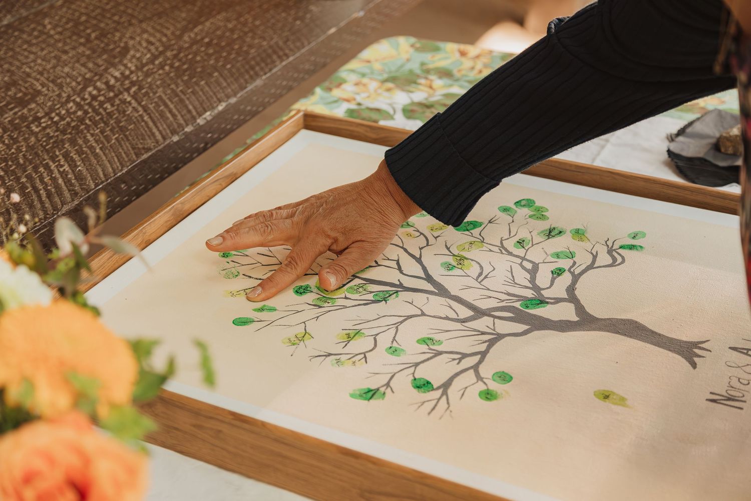 Guest adding fingerprint leaves to a hand-drawn tree illustration in a wedding guestbook.