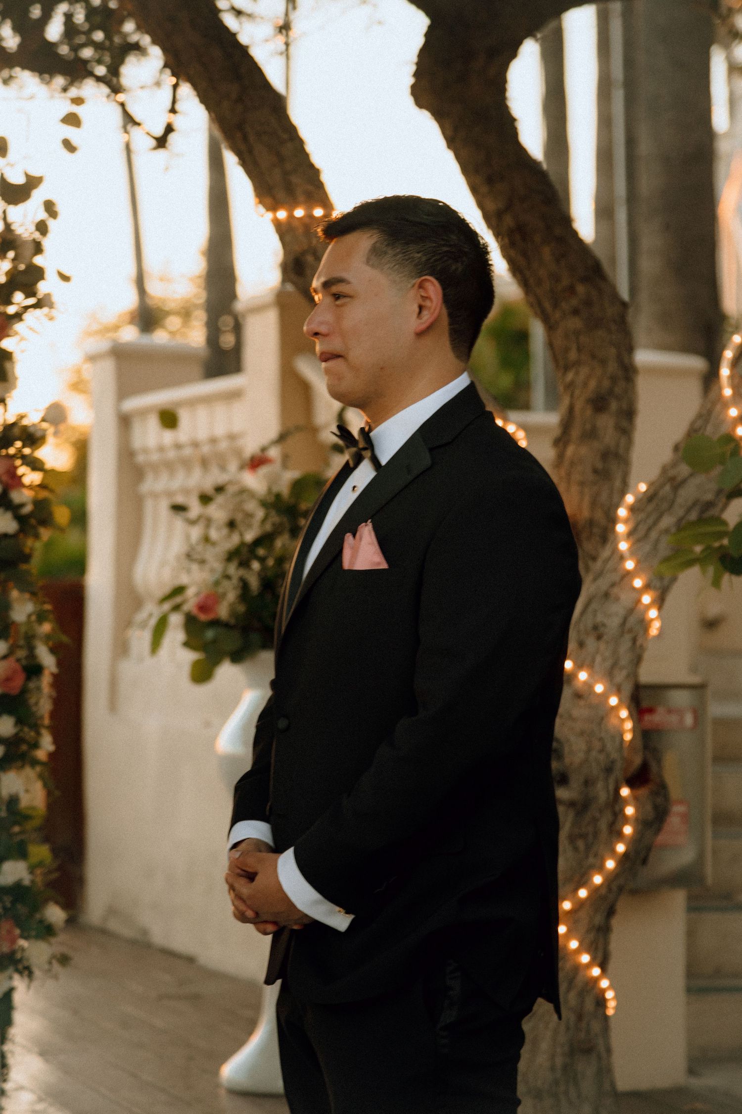 Evening wedding portrait by a garden wall with twinkling lights and tropical trees.