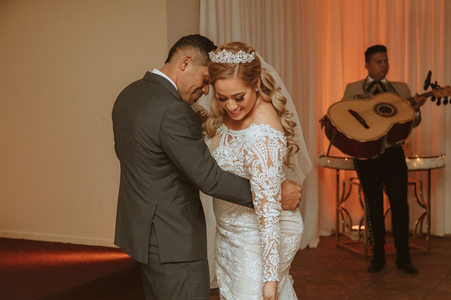 A tender dance moment at a wedding reception with a guitarist performing in the background.
