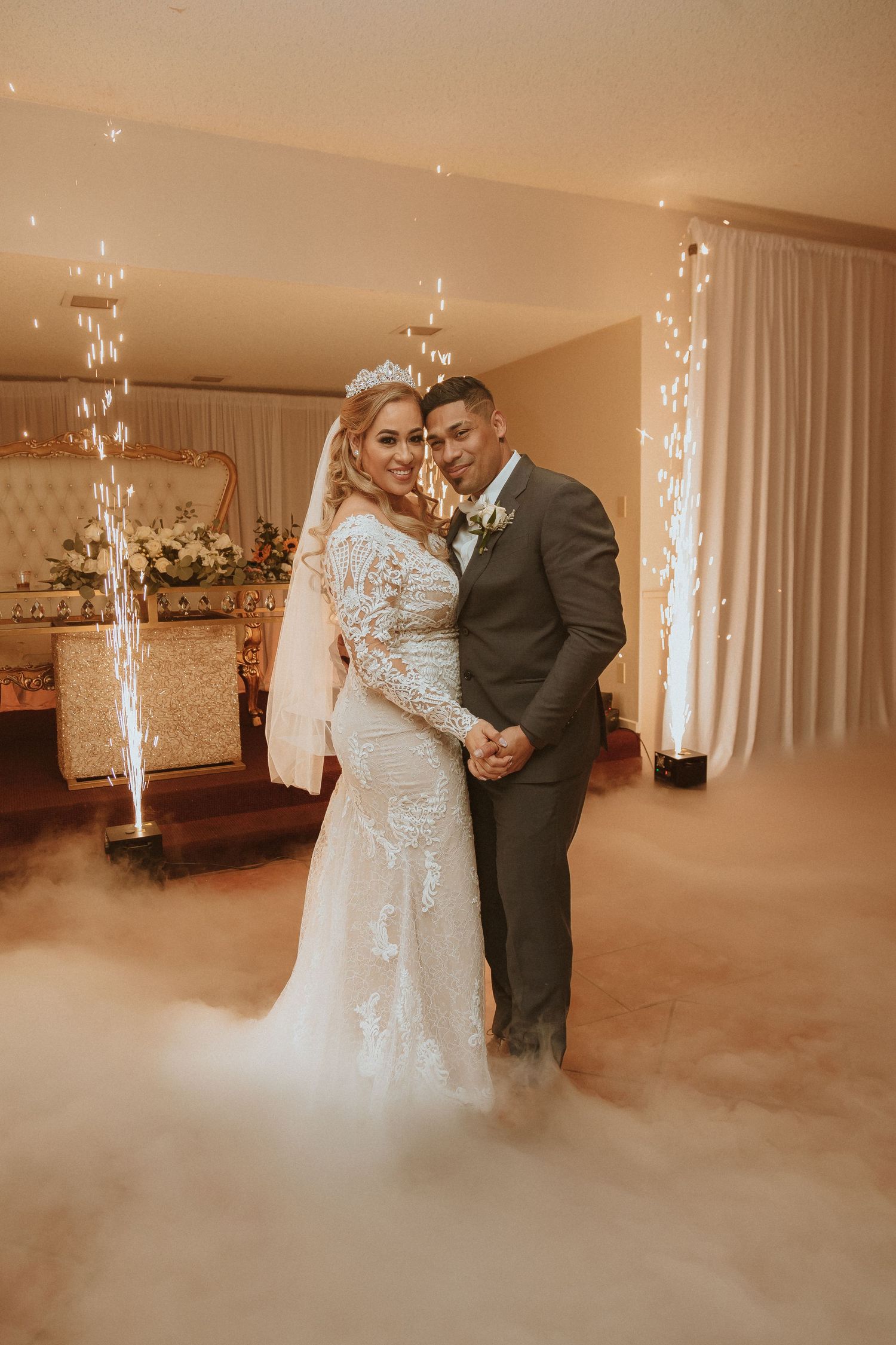A wedding couple poses together in a beautifully decorated venue with dramatic fog effects and sparkling lights.