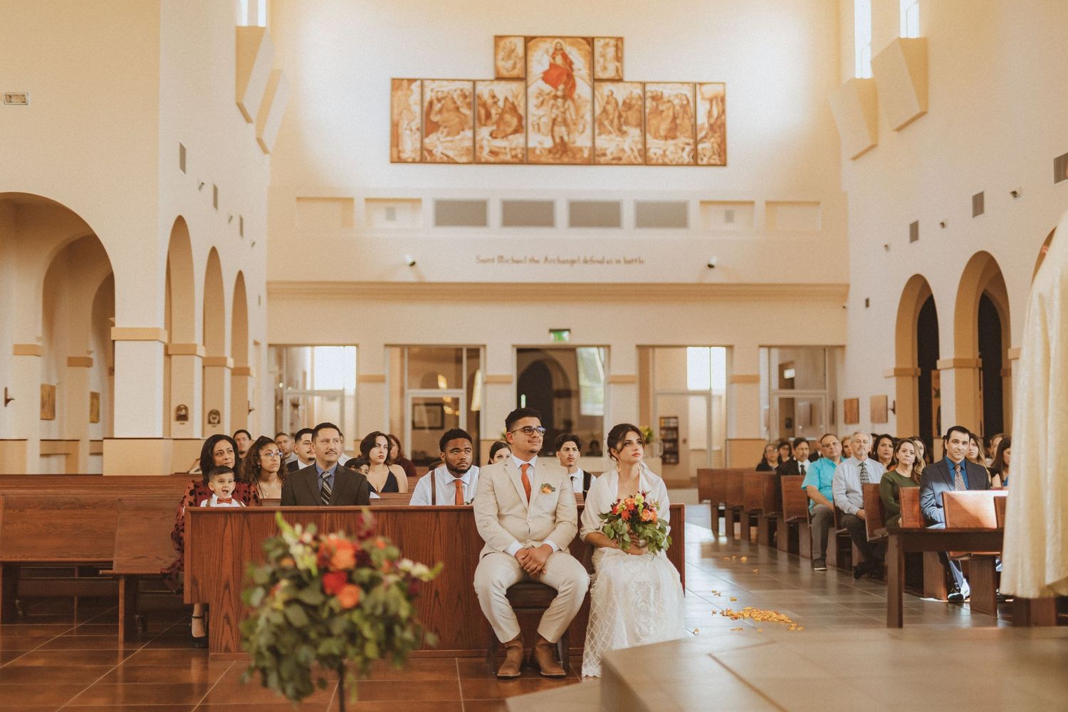 Wide view of a church interior during a wedding ceremony with guests seated in wooden pews.