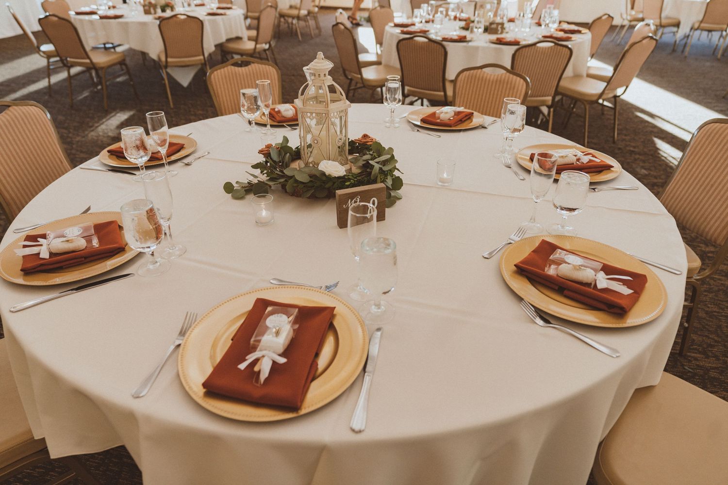 Elegant wedding reception table setting with white linens, gold chargers and burgundy napkins.
