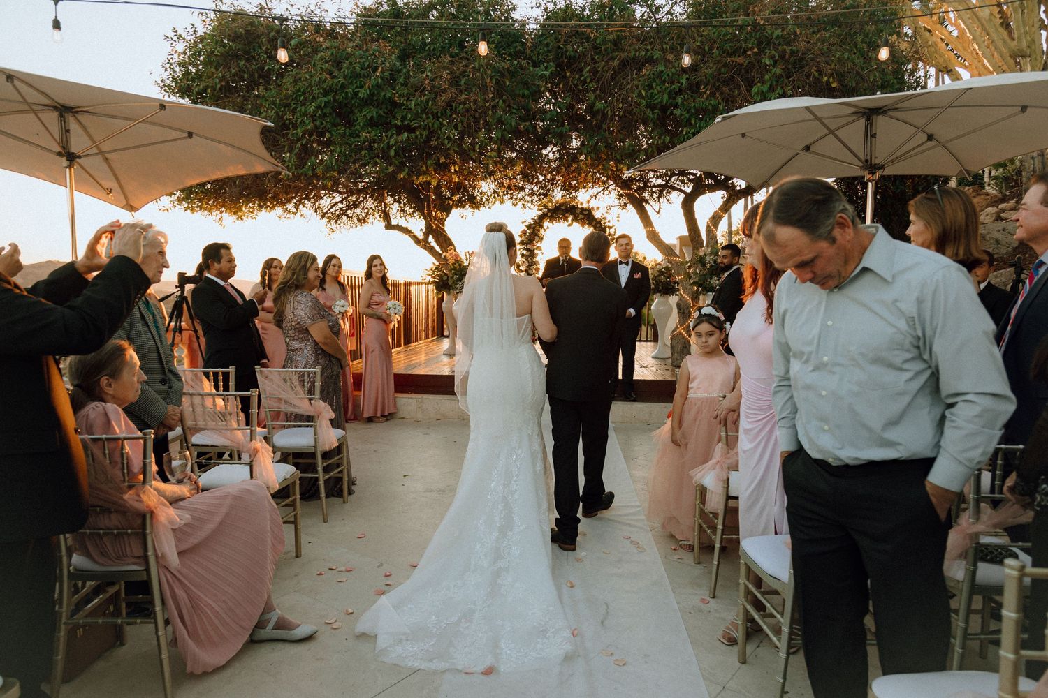A beautiful outdoor wedding ceremony with guests seated under market lights and trees.