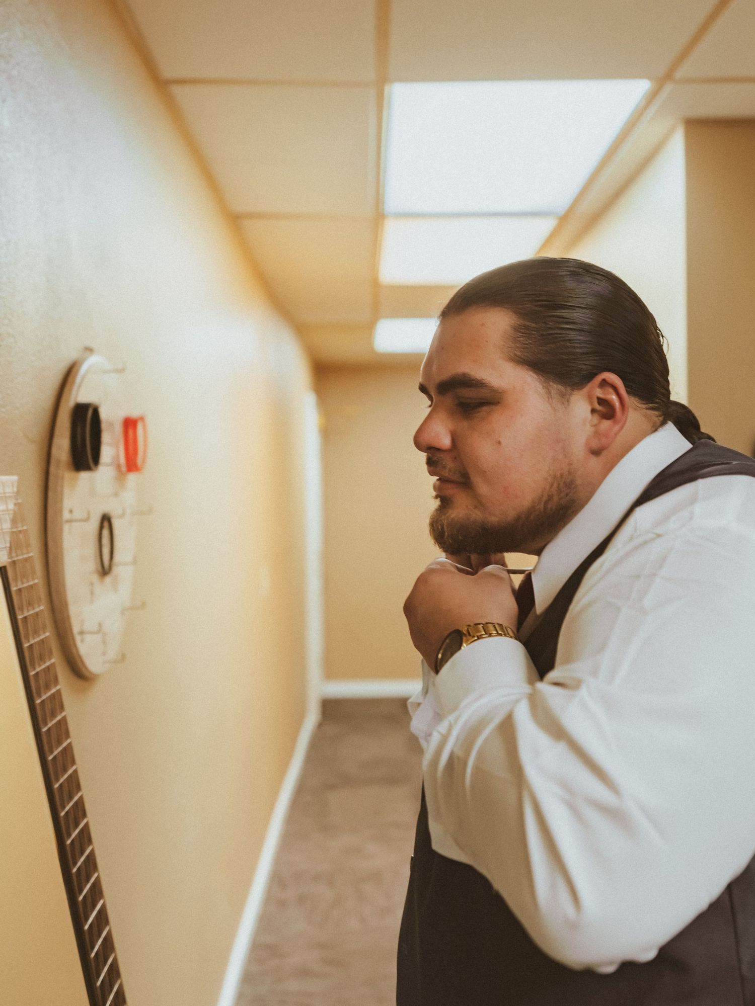 Person in formal vest looks thoughtfully at wall while preparing for event.