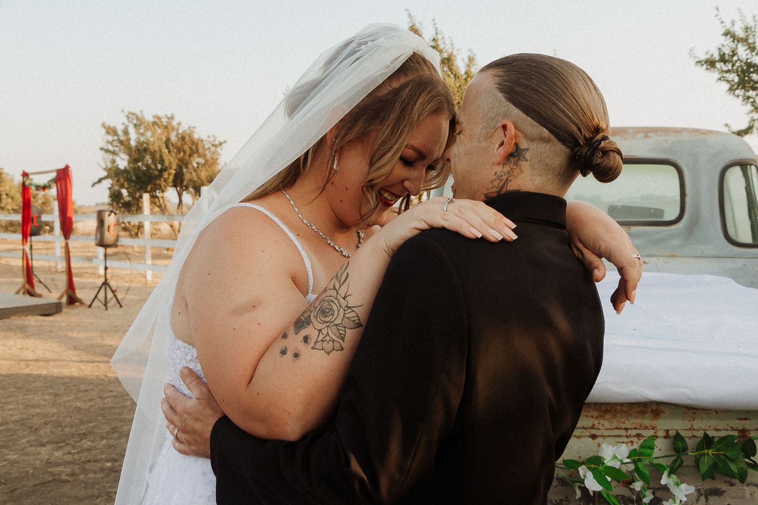 Newlyweds share an intimate moment in front of a vintage truck during their rustic outdoor wedding celebration.