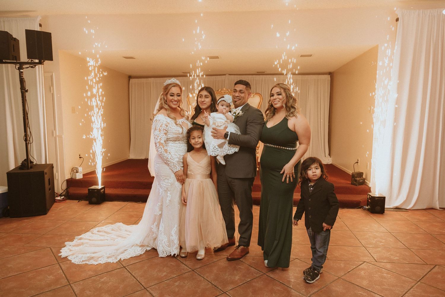 Wedding group portrait featuring formal attire and sparkler effects in a warmly lit venue.