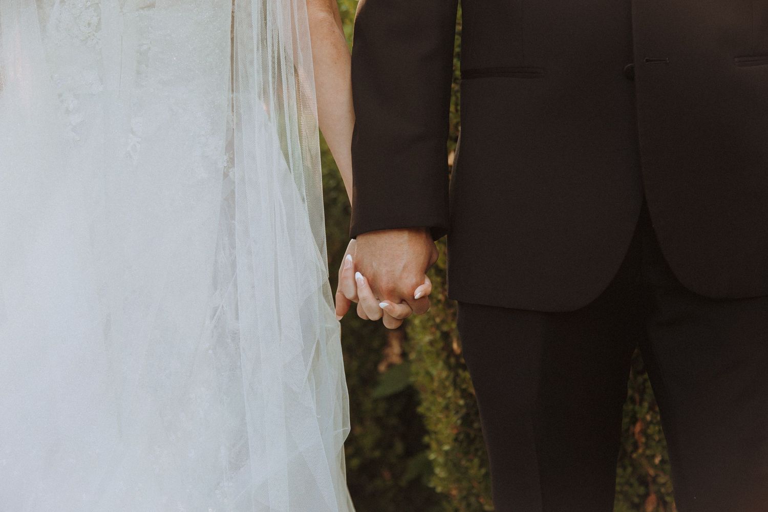 Close-up shot of newlyweds holding hands outdoors.