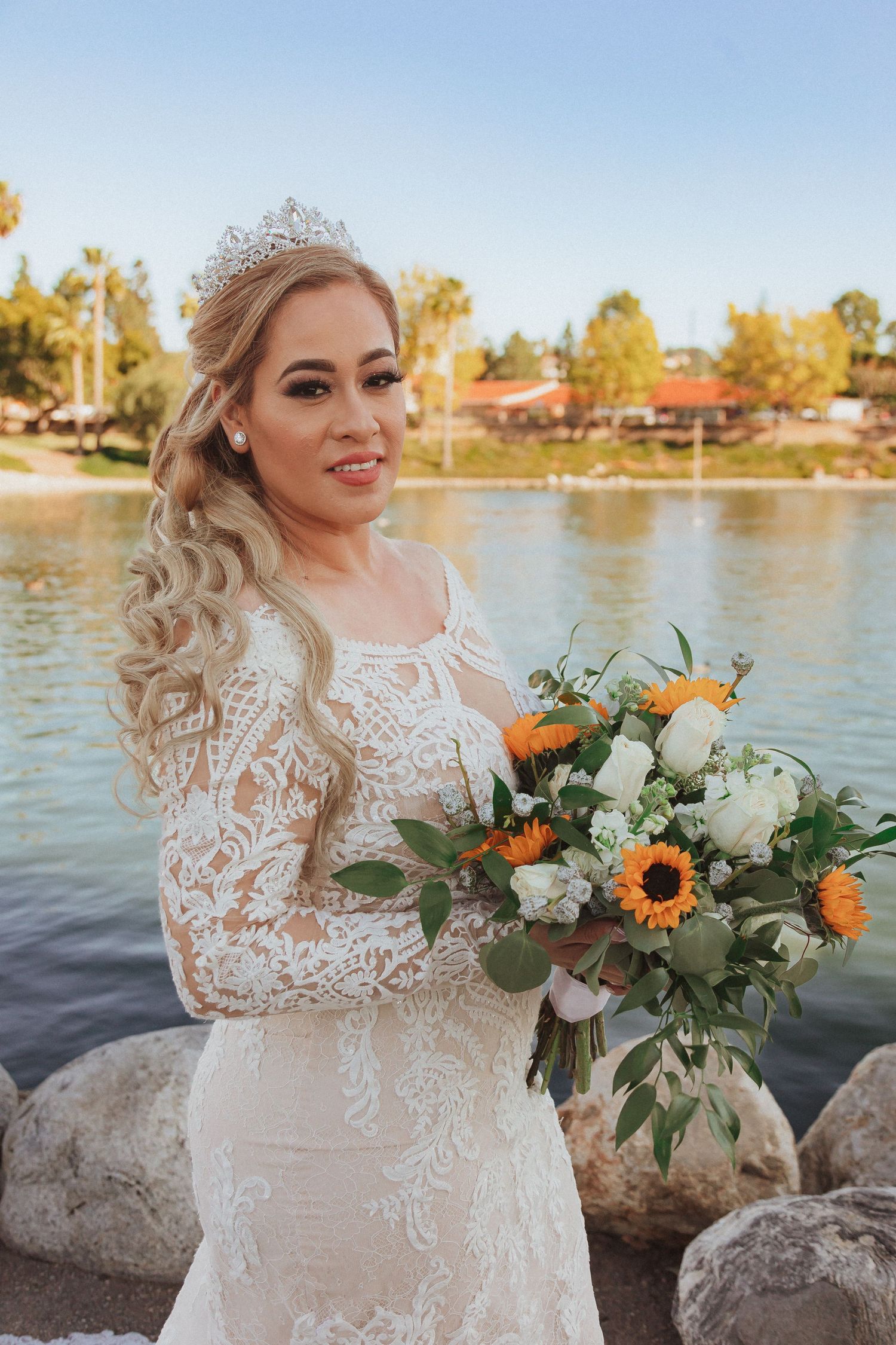 Close-up of bride with sunflower bouquet and lace dress by scenic lake.