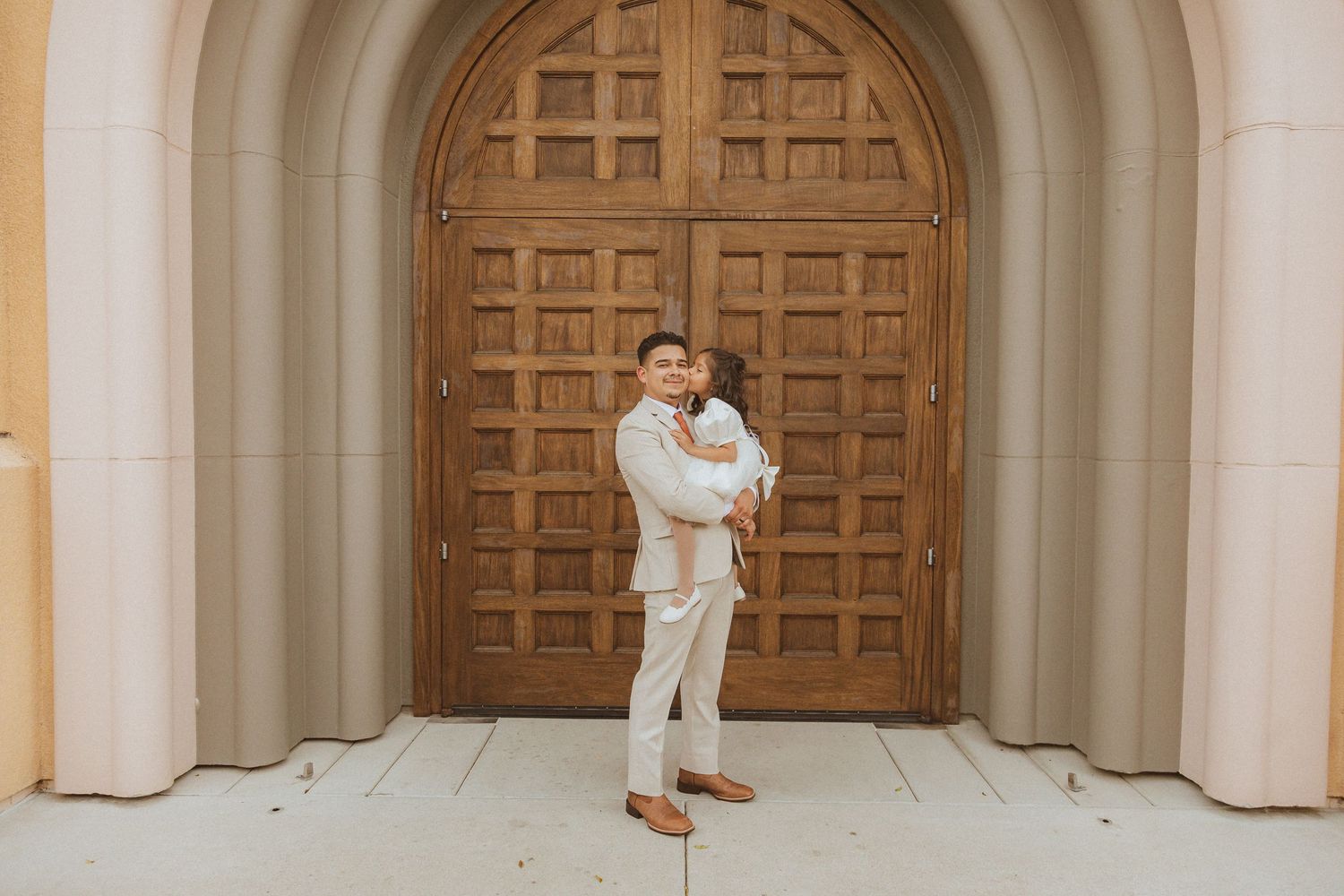 Wedding portrait against ornate wooden doors featuring cream-colored formal attire.