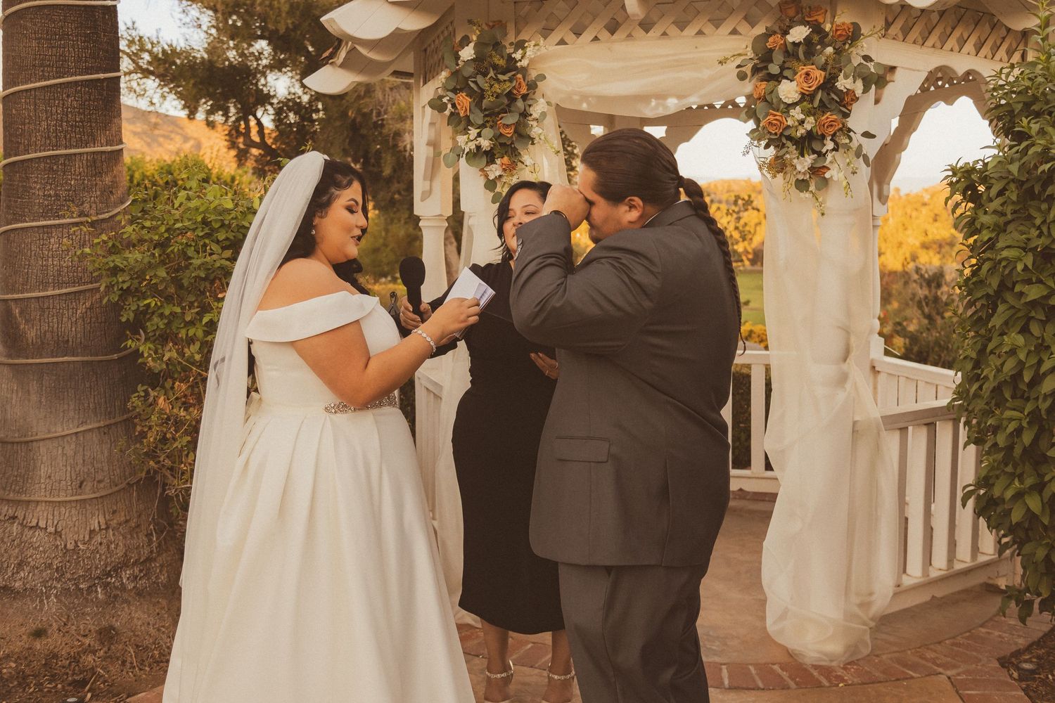 Couple shares heartfelt moment during wedding ceremony under decorated gazebo.