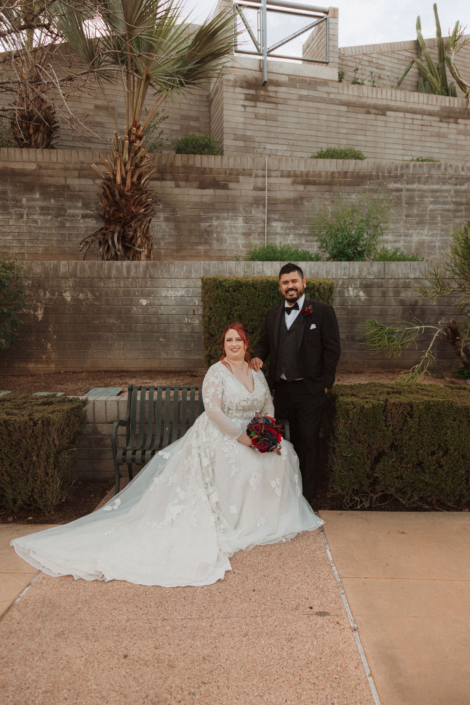 Bride and groom pose for wedding portrait near terraced wall with desert landscaping.