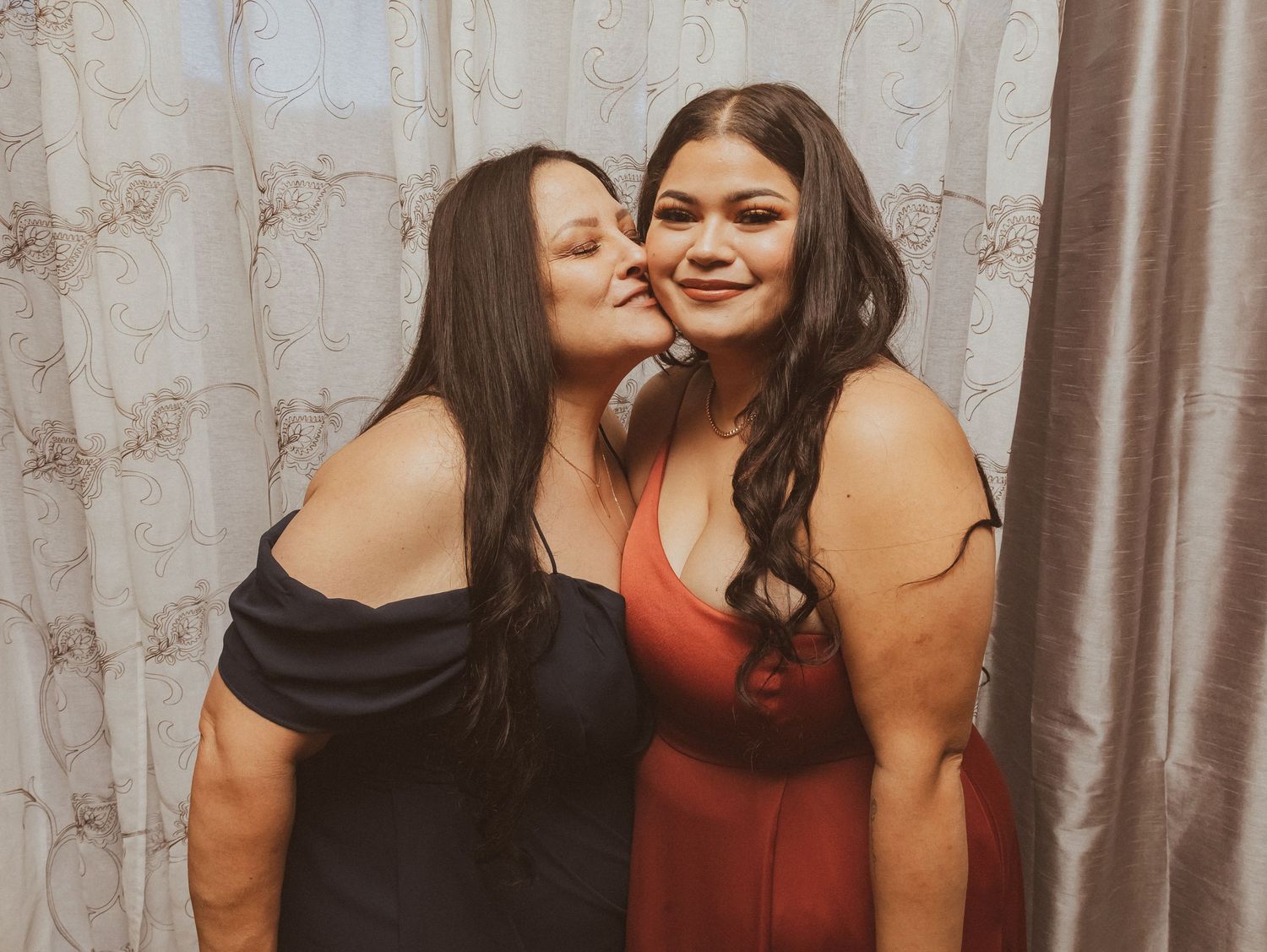 Two friends share an affectionate moment while wearing formal dresses in red and black.