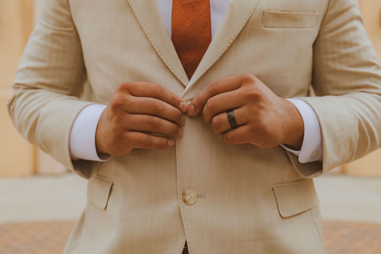 Close up of groom's hands adjusting his beige suit jacket showing wedding ring.