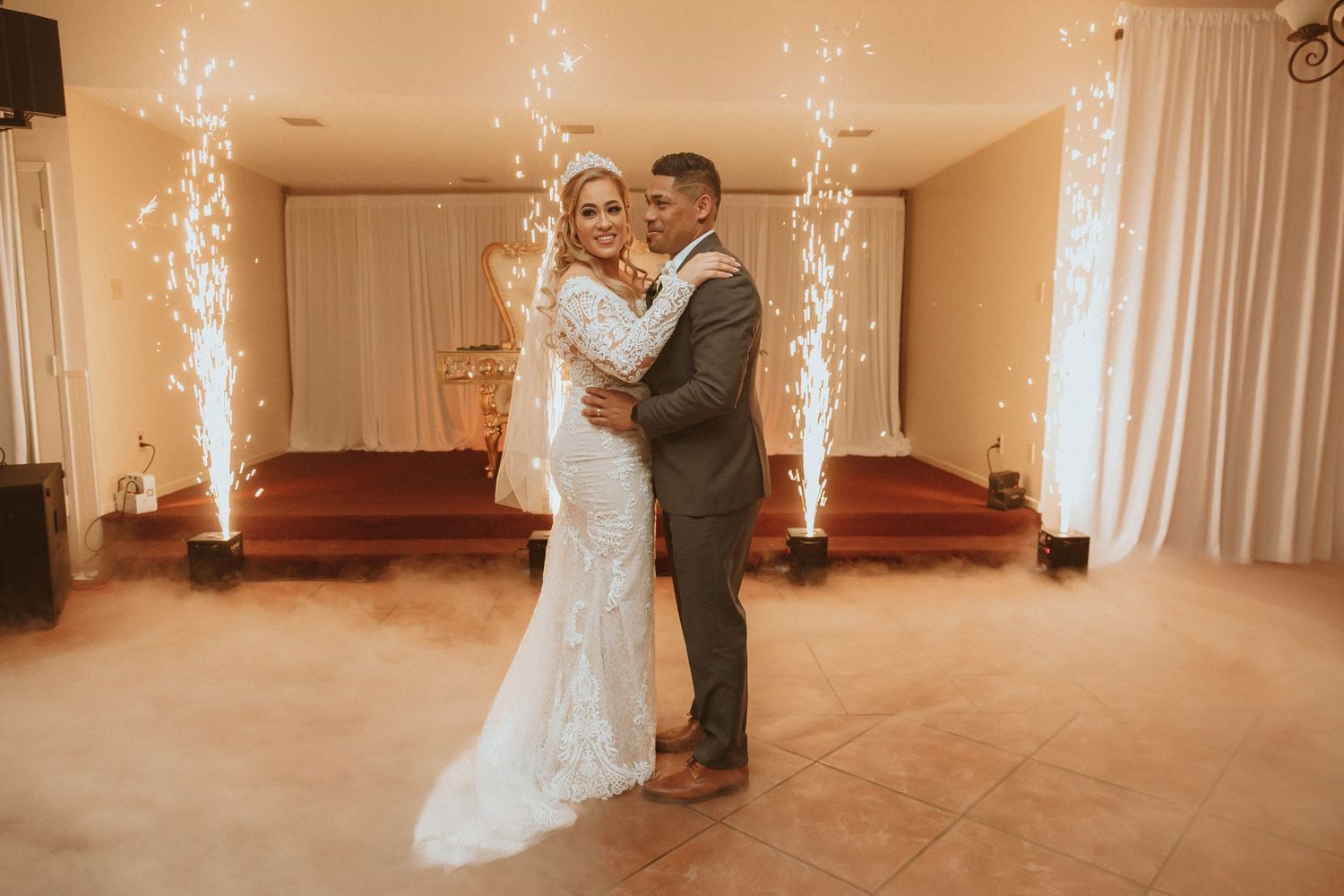 A couple shares their first dance at their wedding with sparkler fountains illuminating the reception venue.