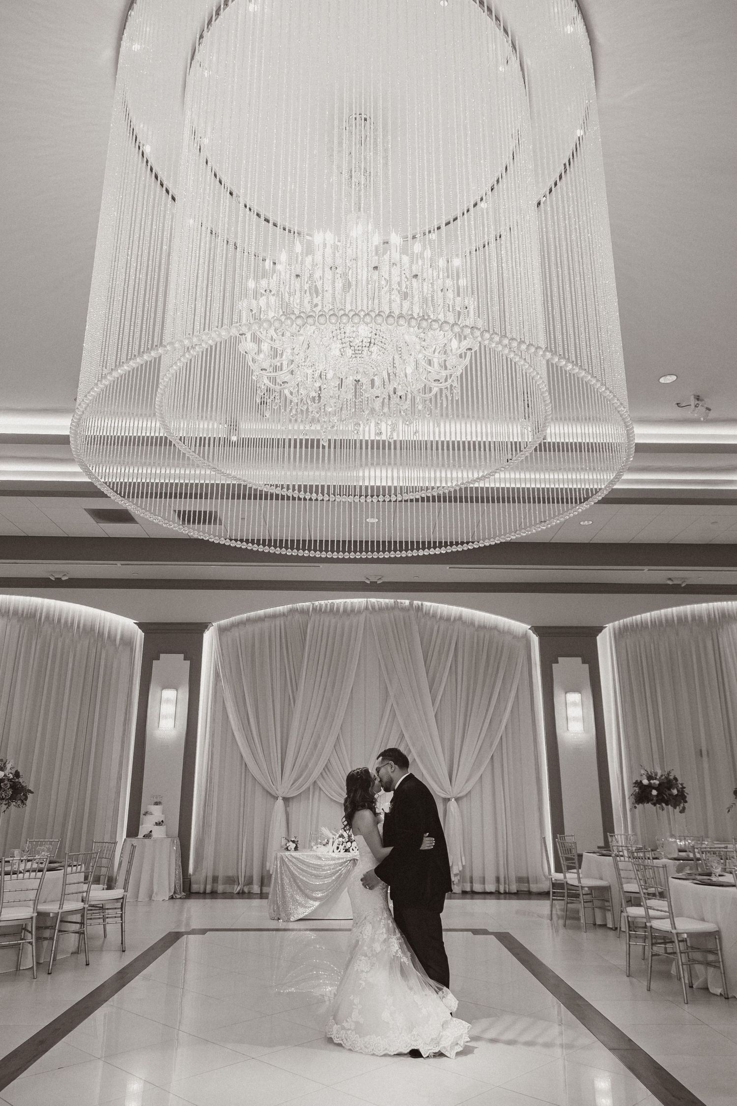 A romantic first dance under an elegant crystal chandelier in a luxurious white-draped ballroom.