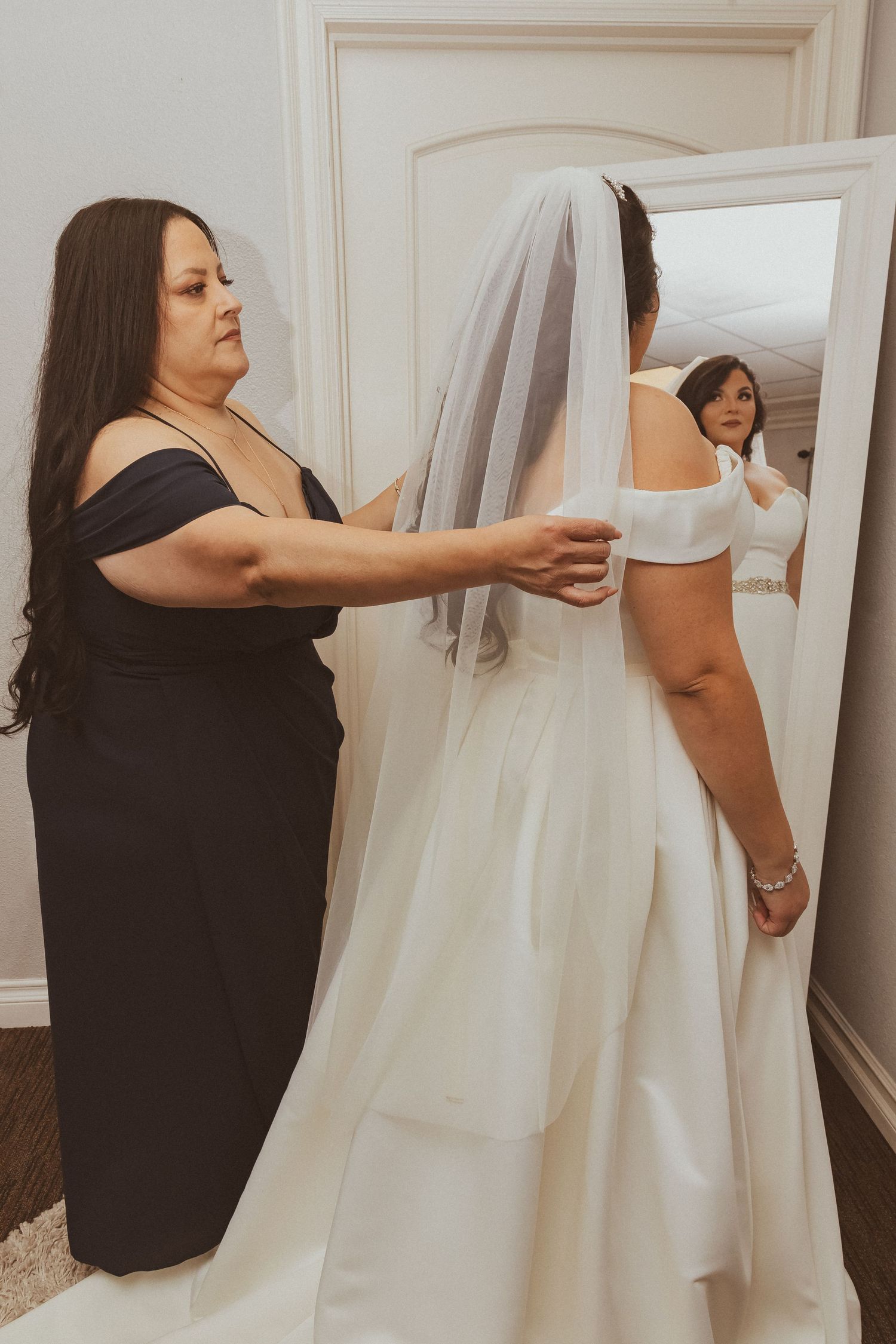 Helper attaching a wedding veil during final bridal preparations.