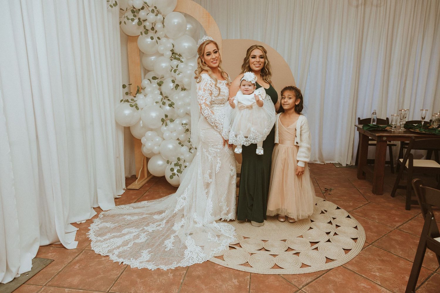 Wedding photo showcasing an elegant white floral arch and beautiful bridal party arrangement.