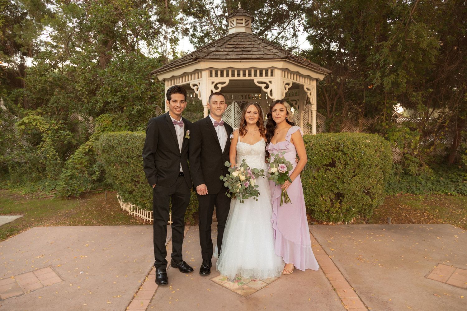 Wedding party poses in front of a garden gazebo at sunset.