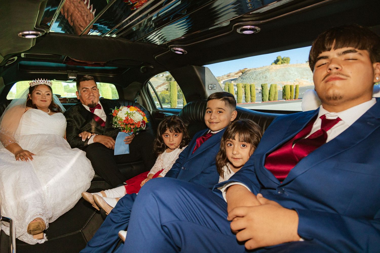 Wedding party relaxes in a black limousine interior with natural lighting.