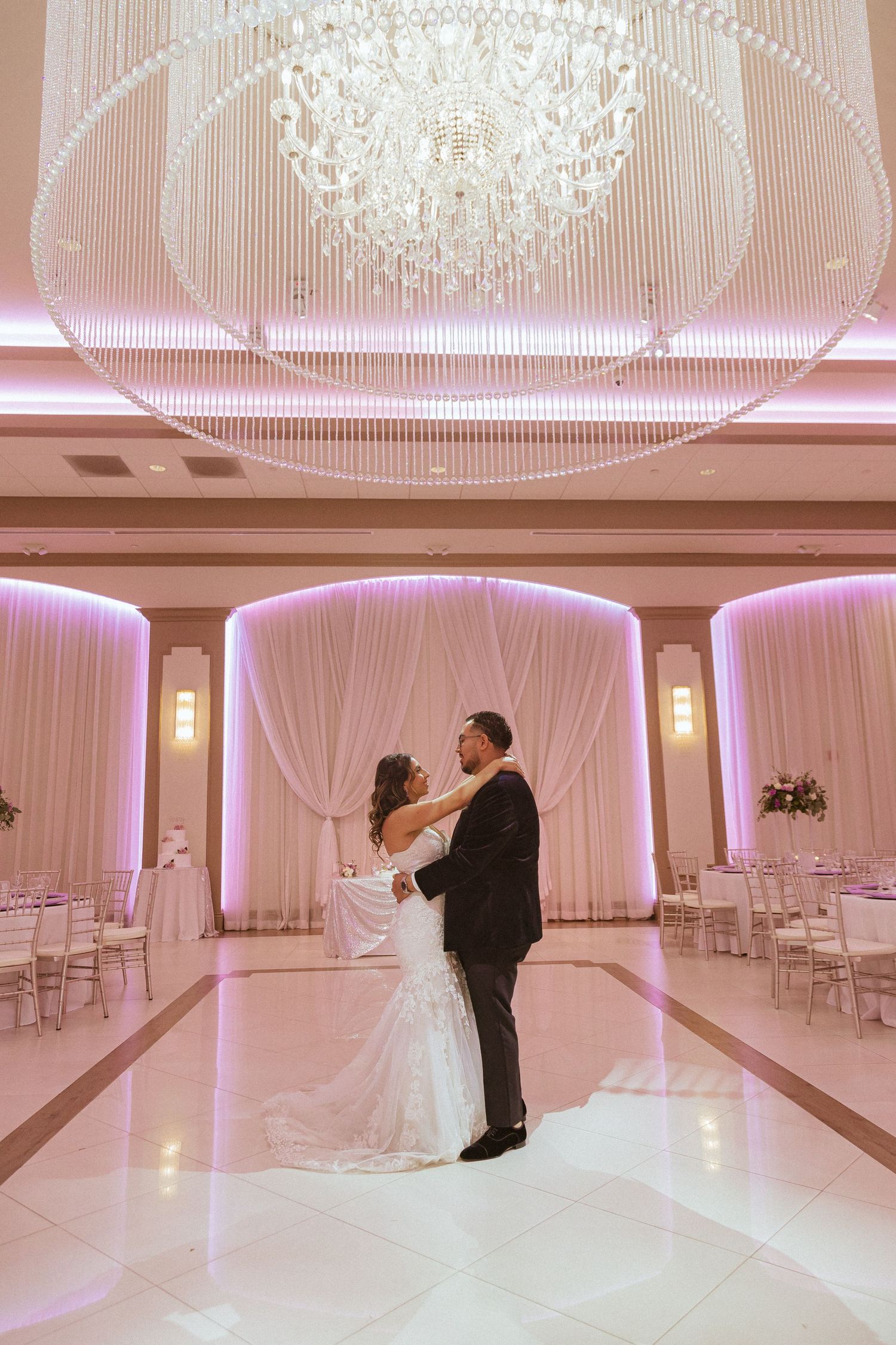 Elegant wedding reception featuring a pink-lit ballroom with a stunning crystal chandelier and draped walls.