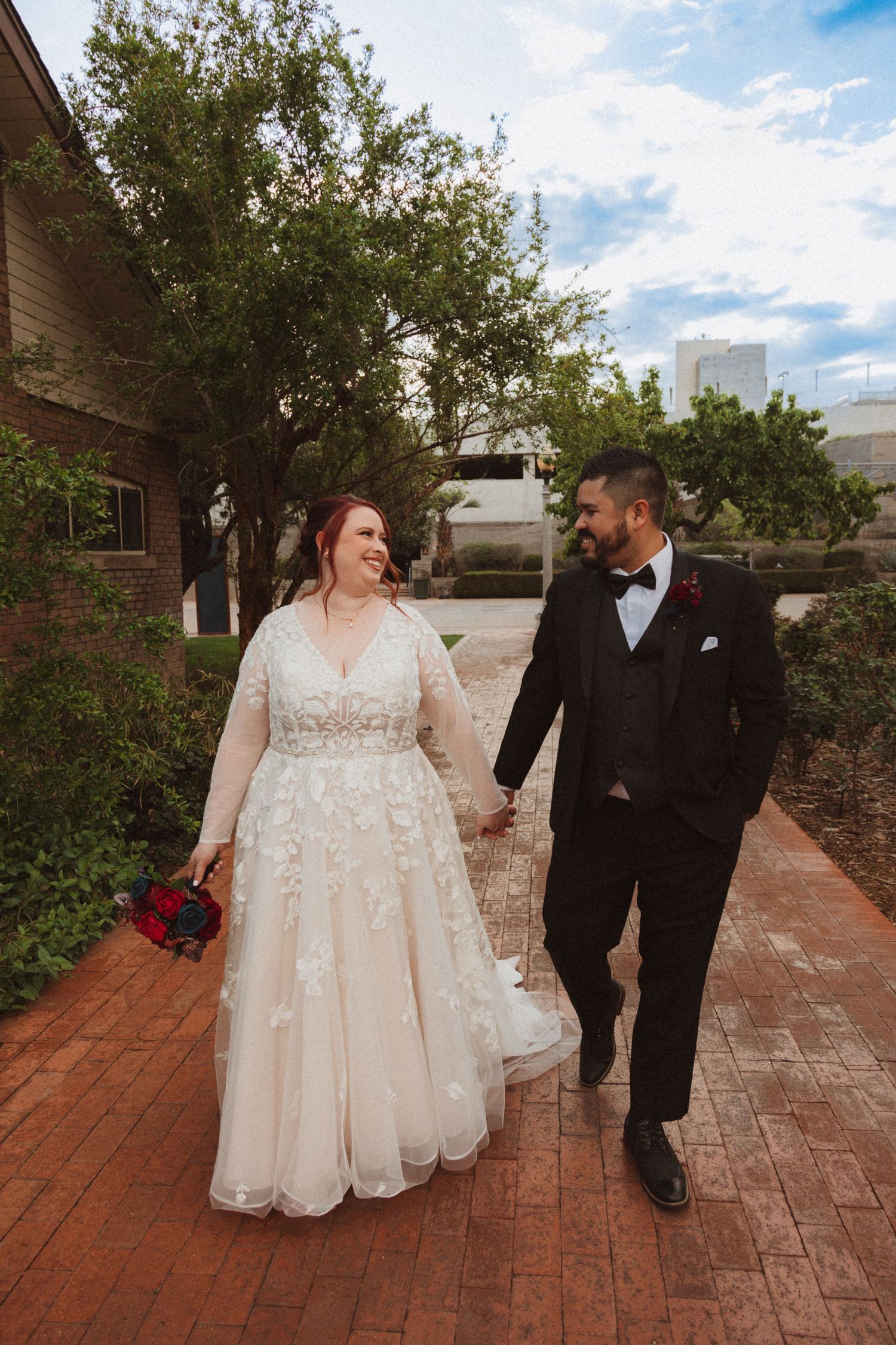 A couple strolls along a landscaped brick pathway during their wedding photoshoot.