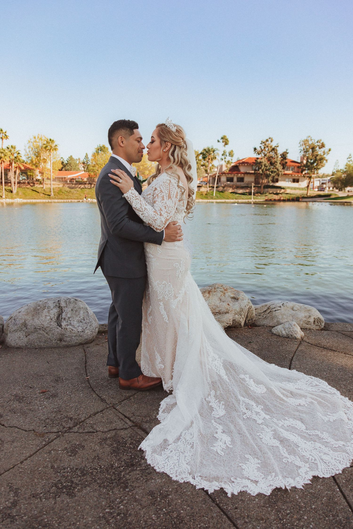 Newlyweds share an intimate moment by the water with a dramatic lace wedding dress train.