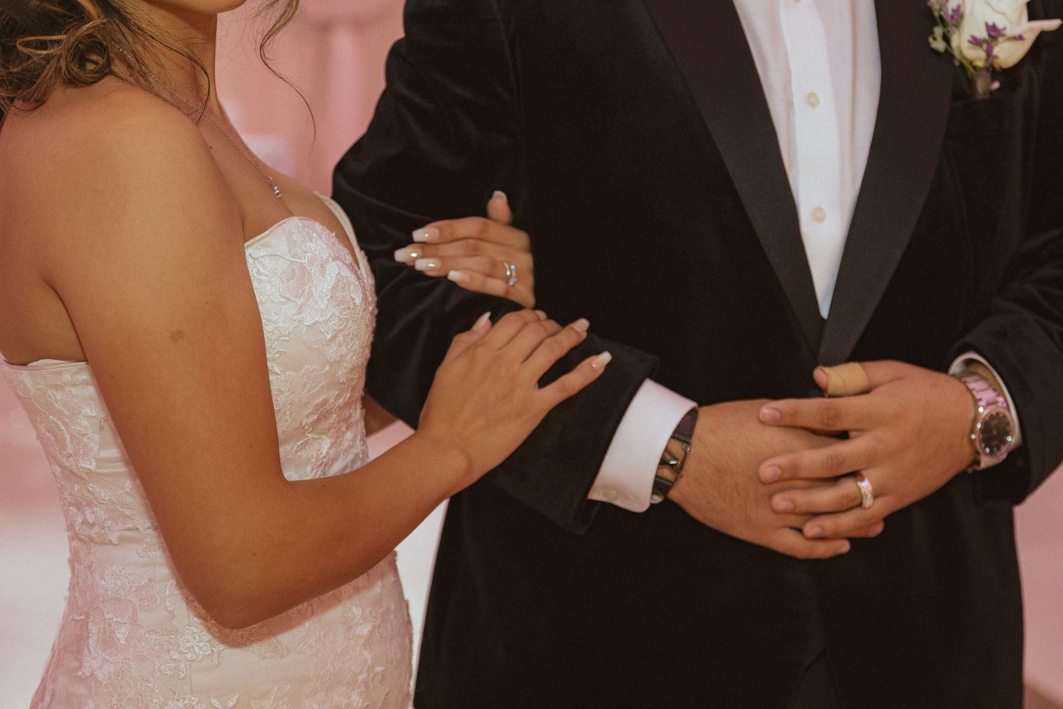 Close-up detail of bride and groom's hands during wedding ceremony in formal attire.