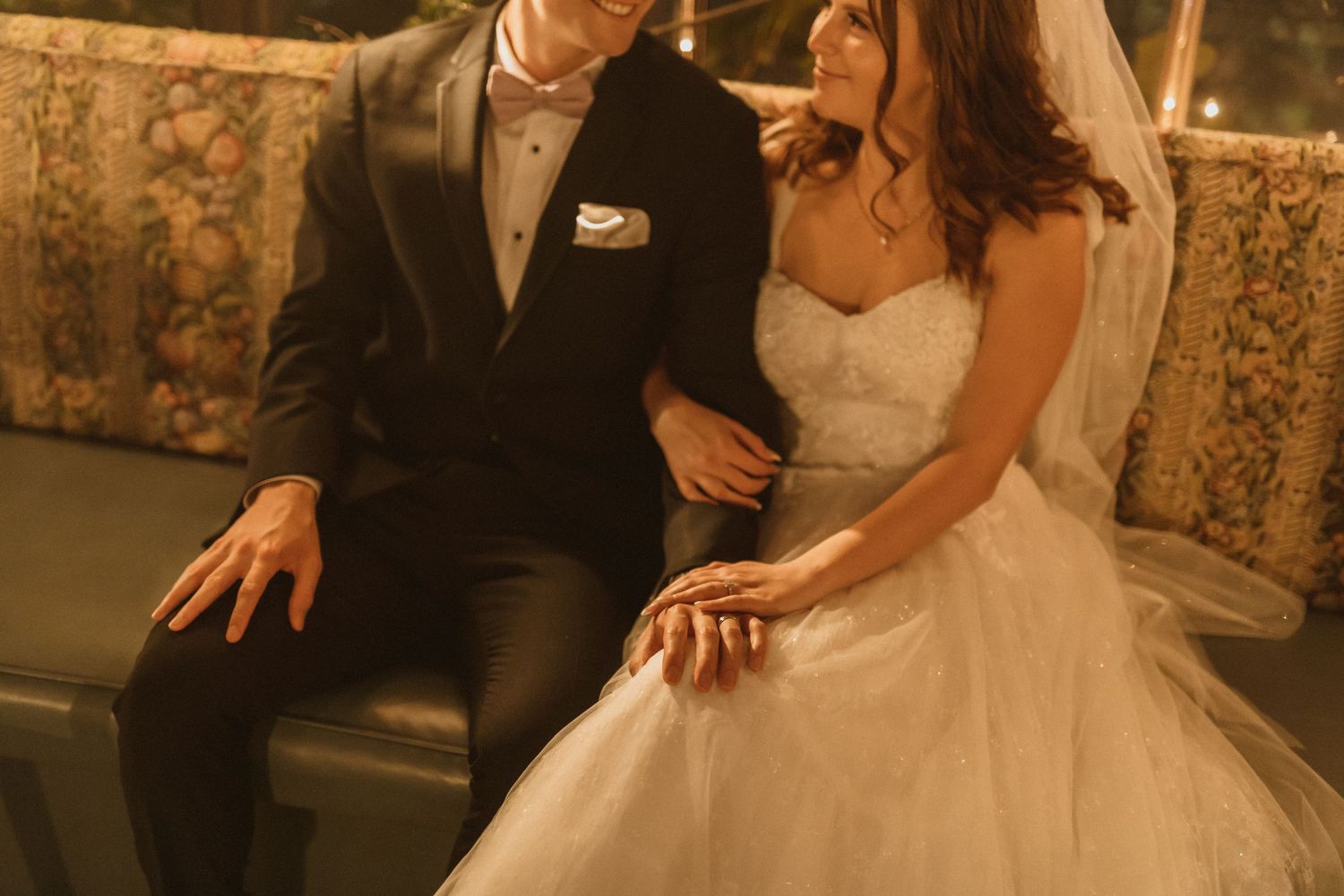Newlywed couple shares intimate moment on vintage sofa in golden evening light.