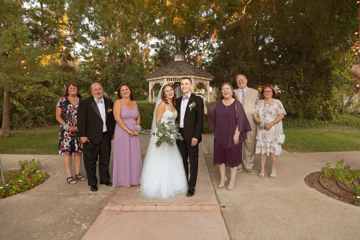 Wedding party group photo on garden path with formal attire and florals.
