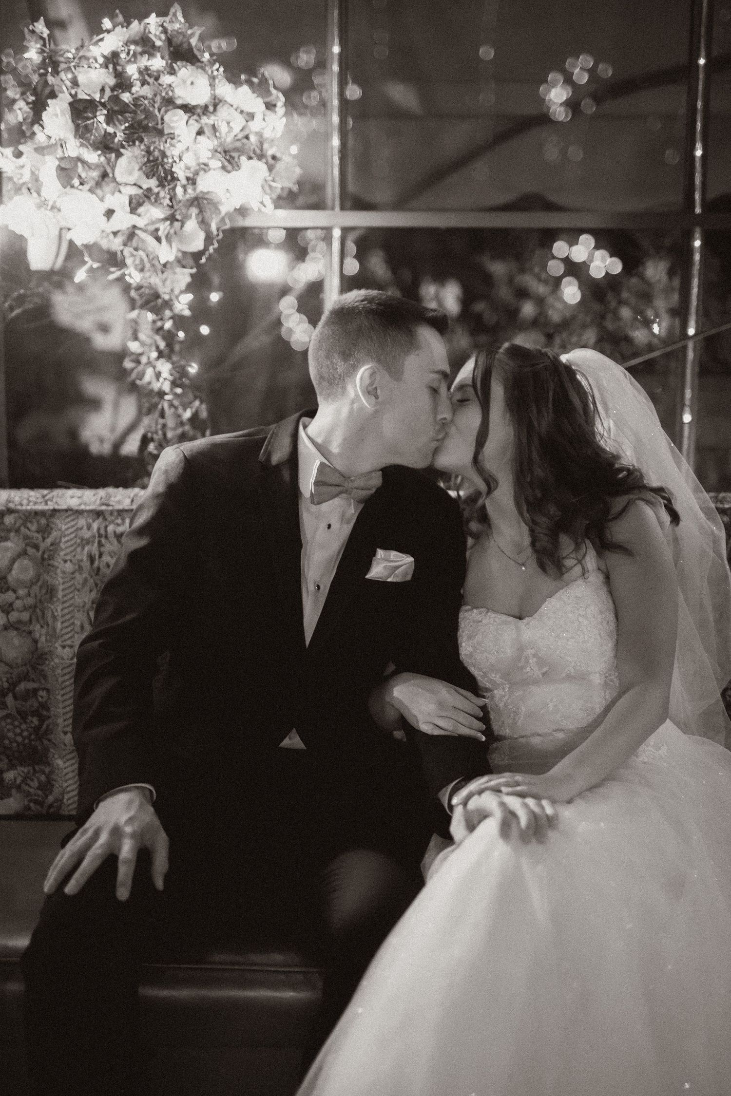 Black and white romantic moment between newlyweds with floral decor in background.