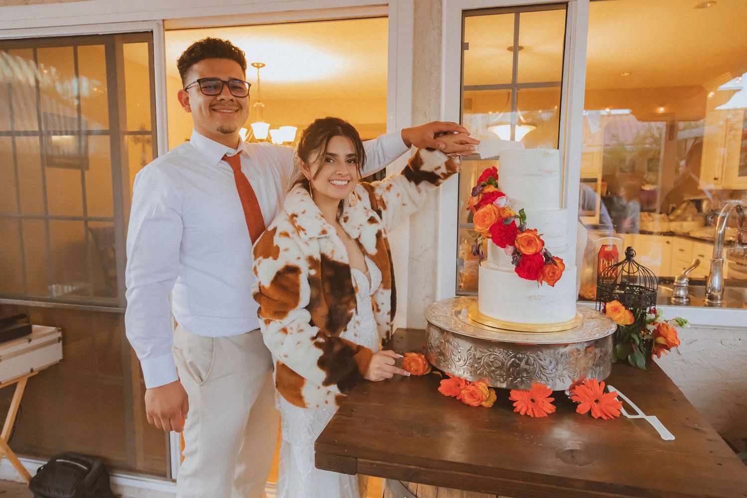 A wedding reception scene with a beautiful tiered cake decorated with coral flowers.