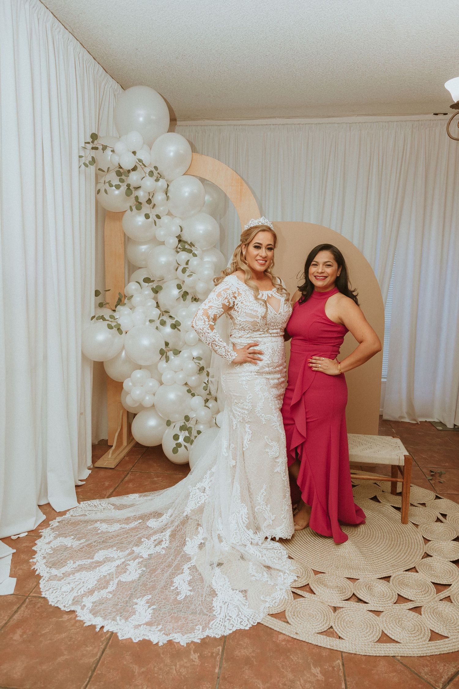 Elegant lace wedding dress with long train photographed with formal red gown against white decor.