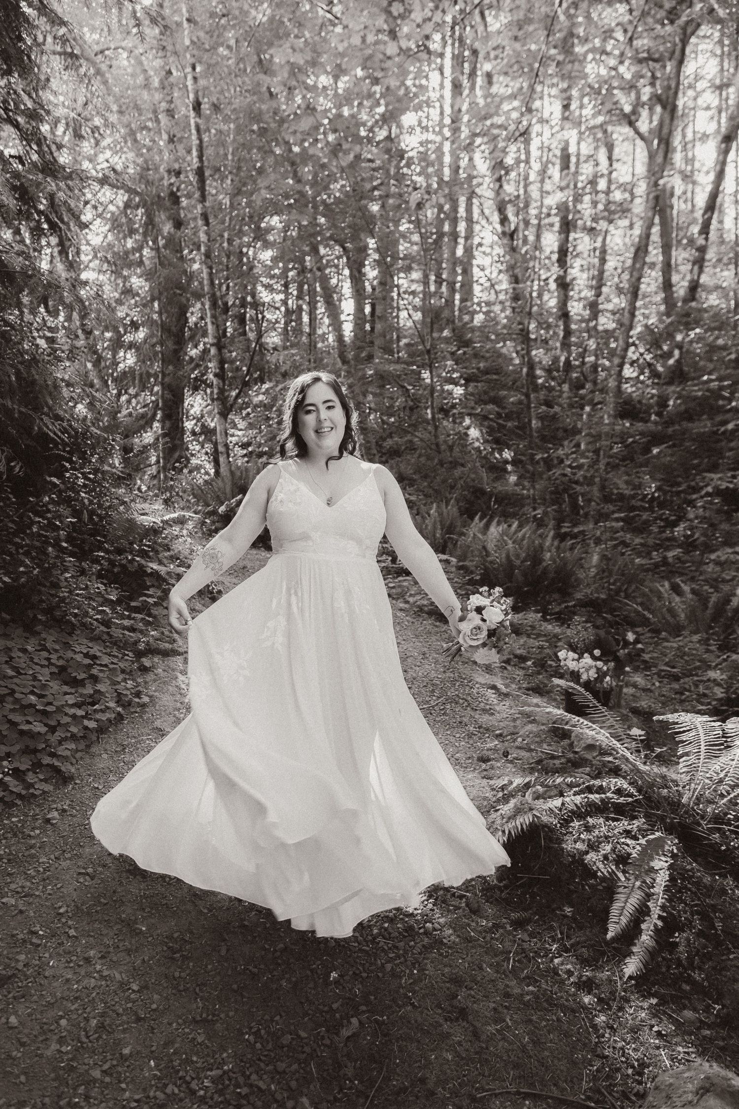 A person in a flowing white wedding dress poses dramatically on a forest path.