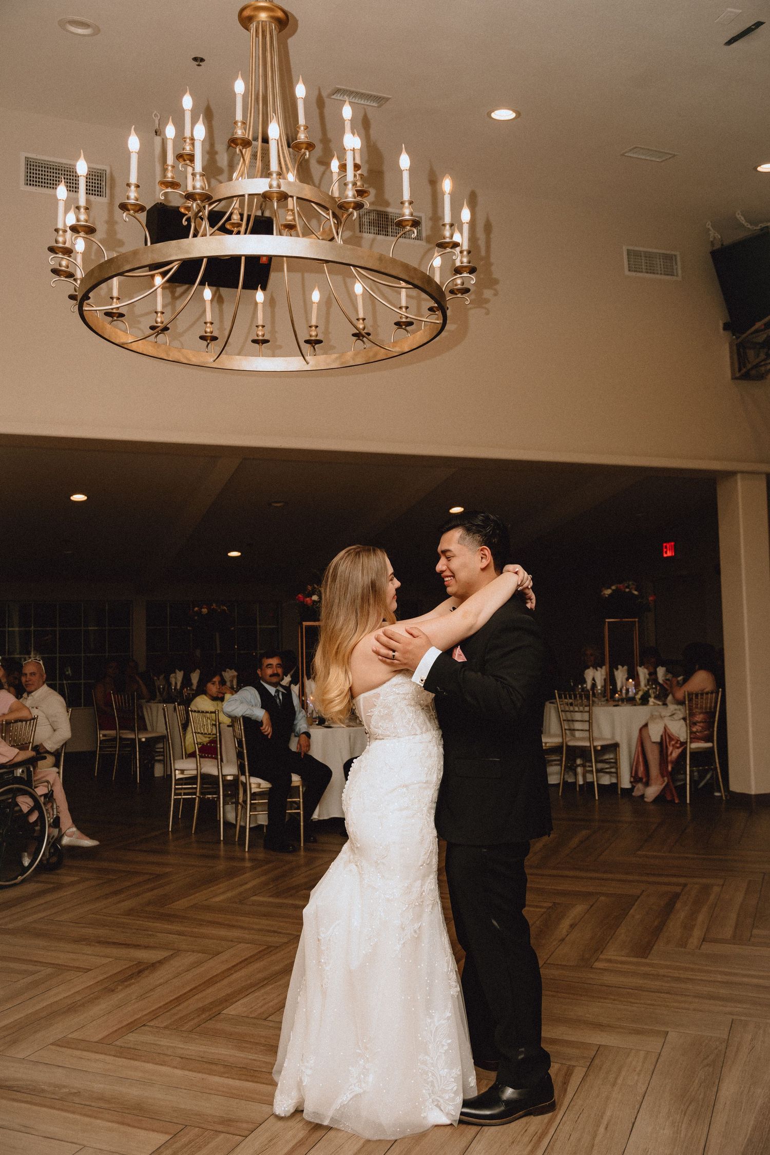A tender first dance moment beneath a grand circular chandelier in an elegant ballroom.